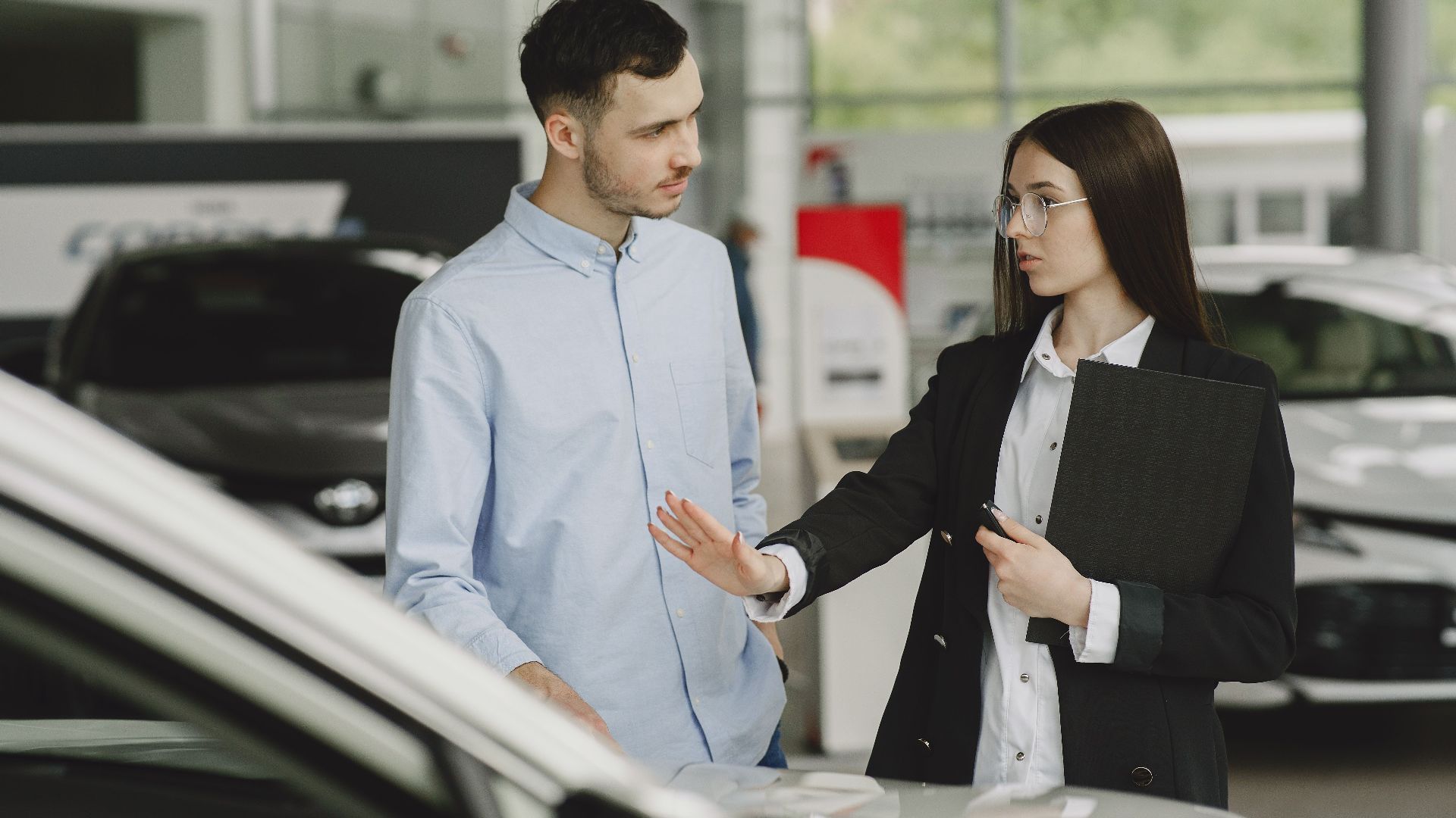 A salesperson and customer discussing car features in a dealership setting.
