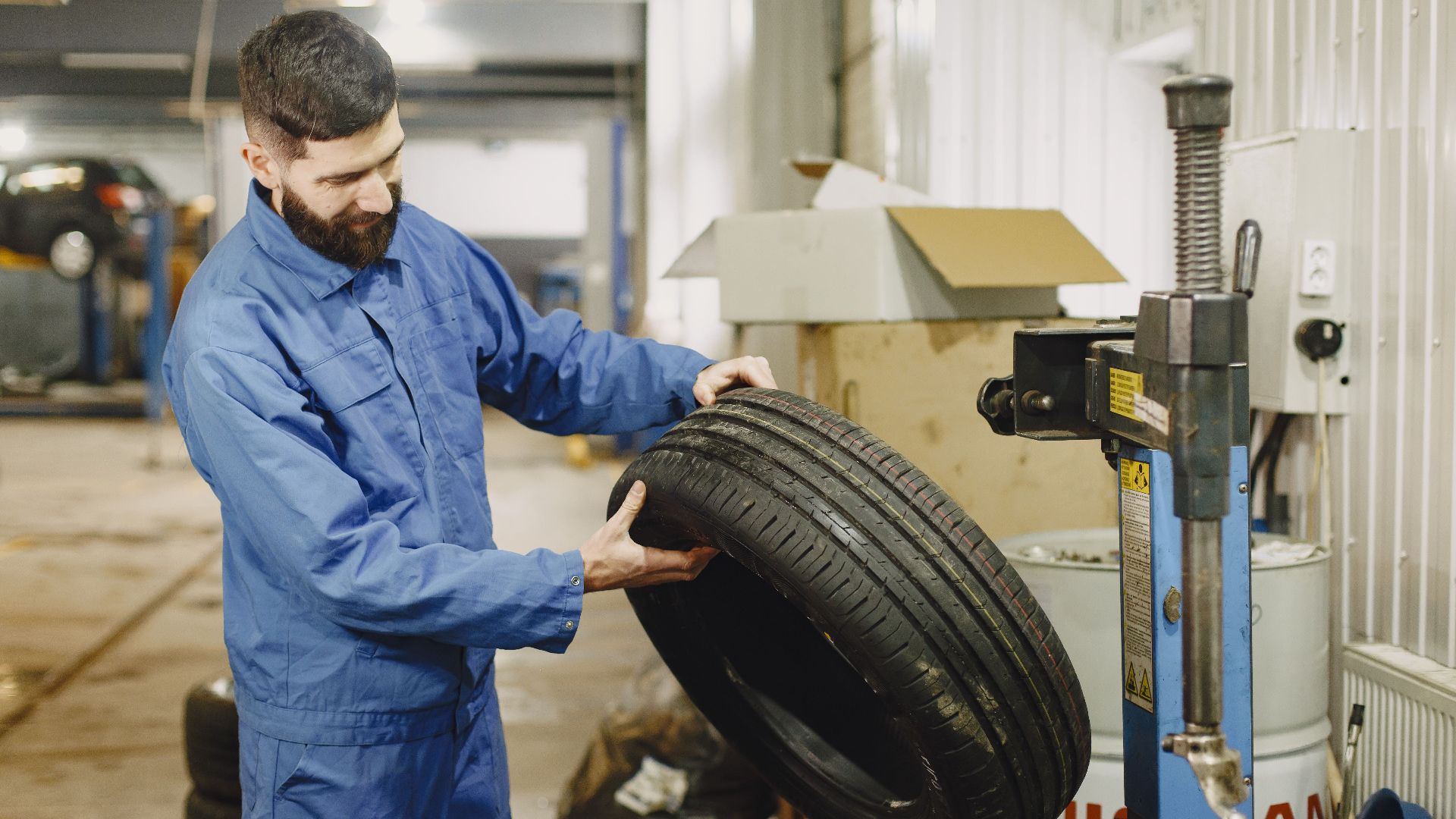 Mechanic in blue uniform examining a tire in an automotive garage.
