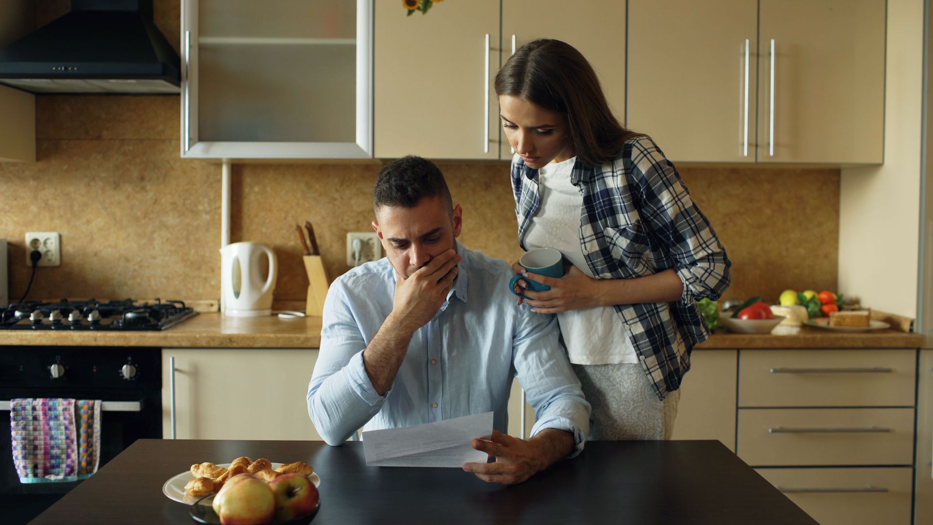 Concerned couple reviewing financial document in modern kitchen setting.