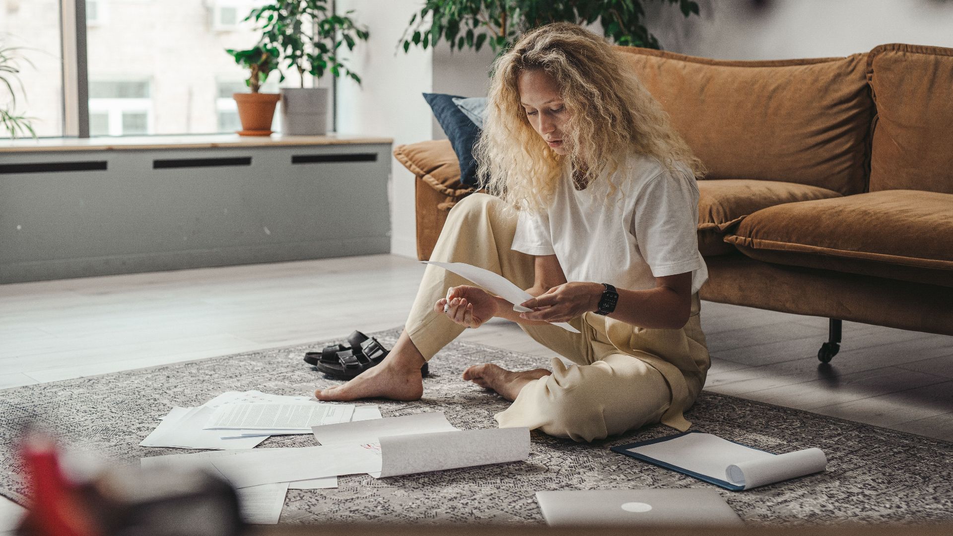 Woman sitting on the floor at home, reviewing paperwork in a relaxed environment.