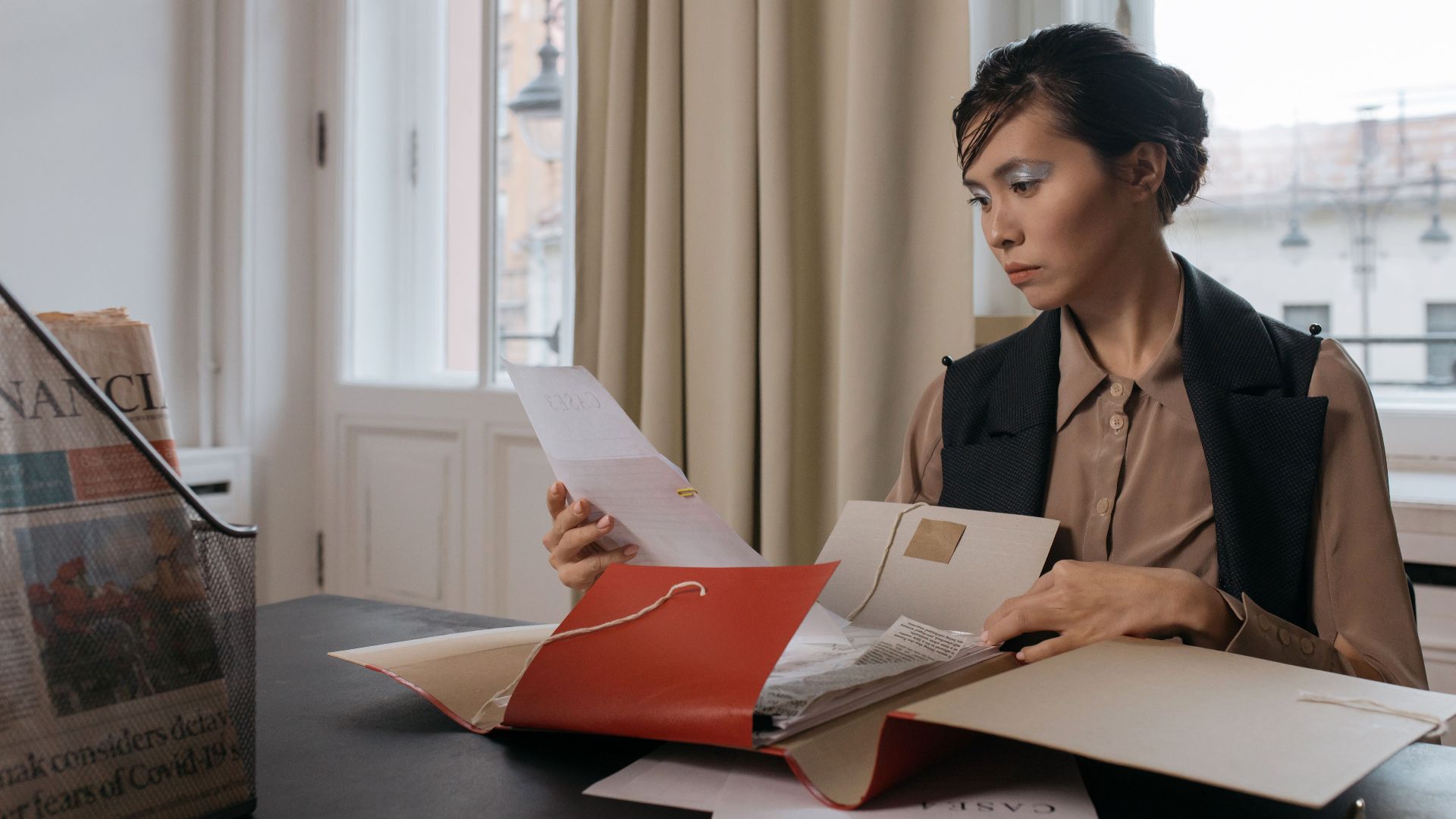 Businesswoman in an office setting reviewing important documents from a red folder with focus and determination.