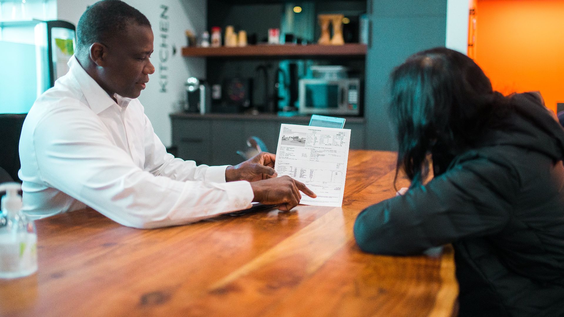 Business meeting between colleagues discussing a document indoors at a wooden table.