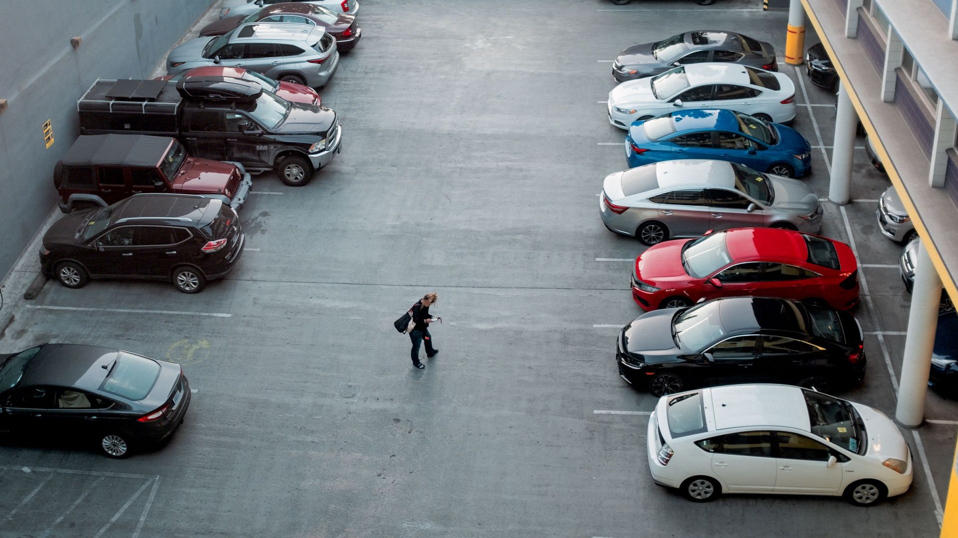 A man walks in a city parking lot filled with various cars, offering a busy urban scene.