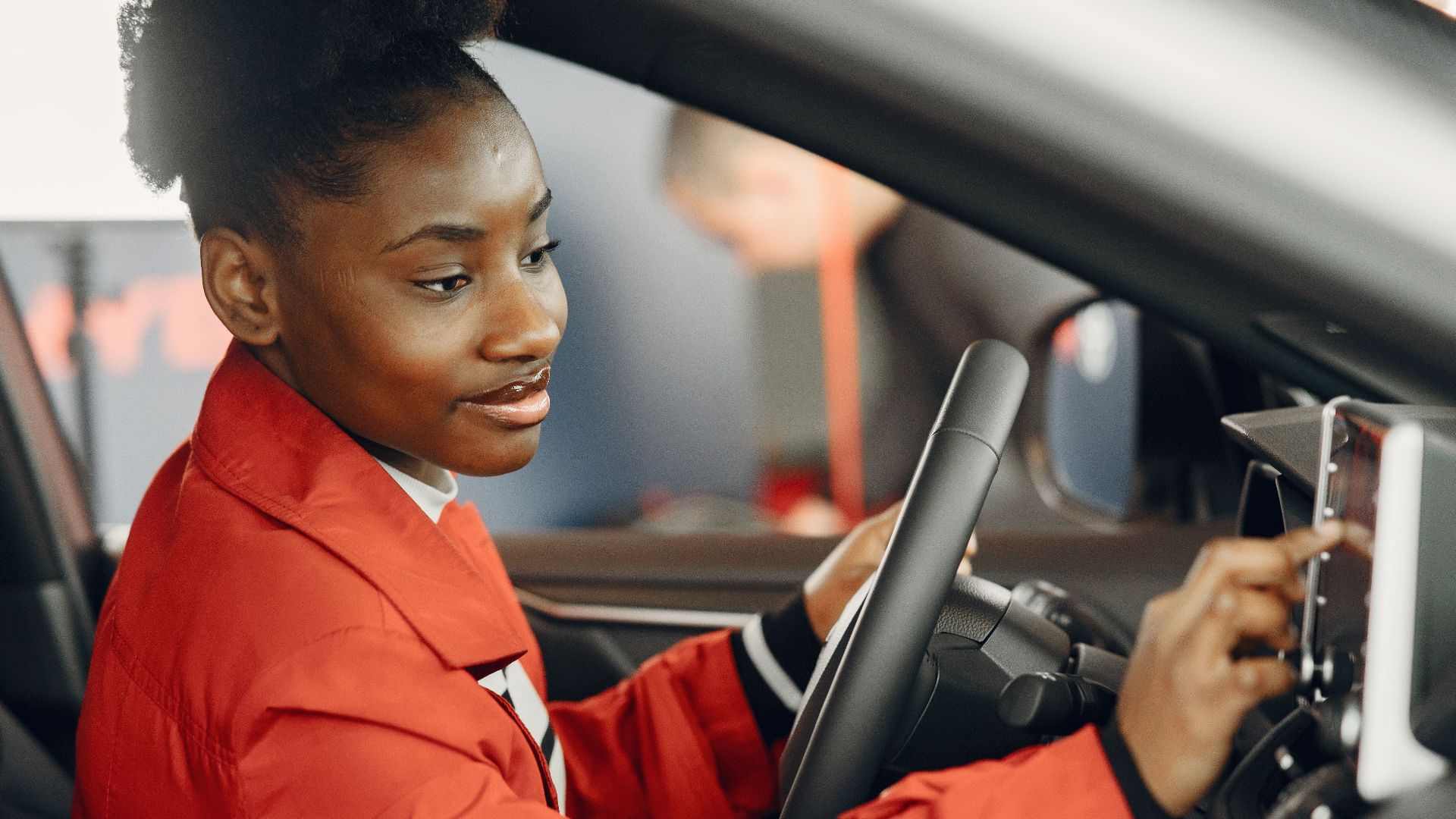 Young woman in red coat using touch screen in car interior.