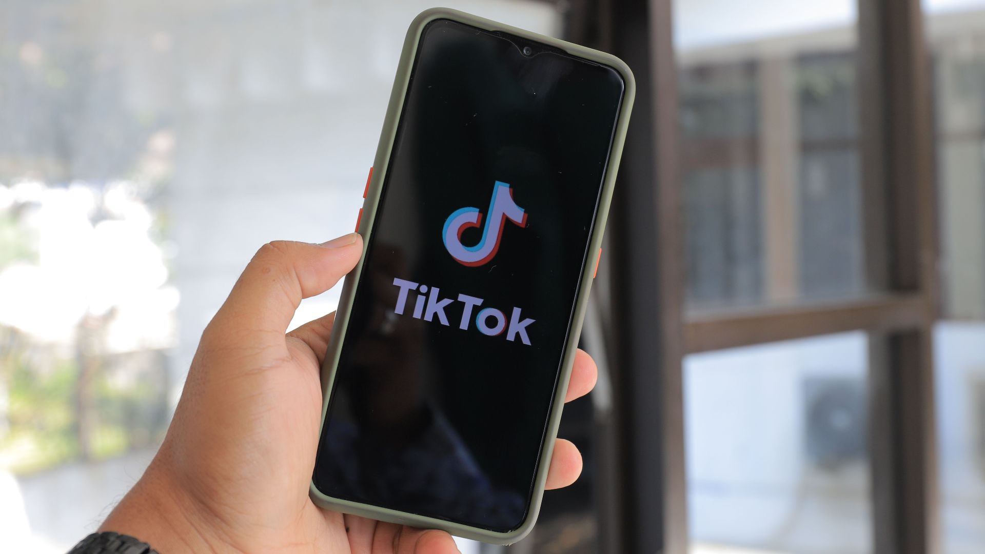 Close-up of a hand holding a smartphone displaying the TikTok app indoors.