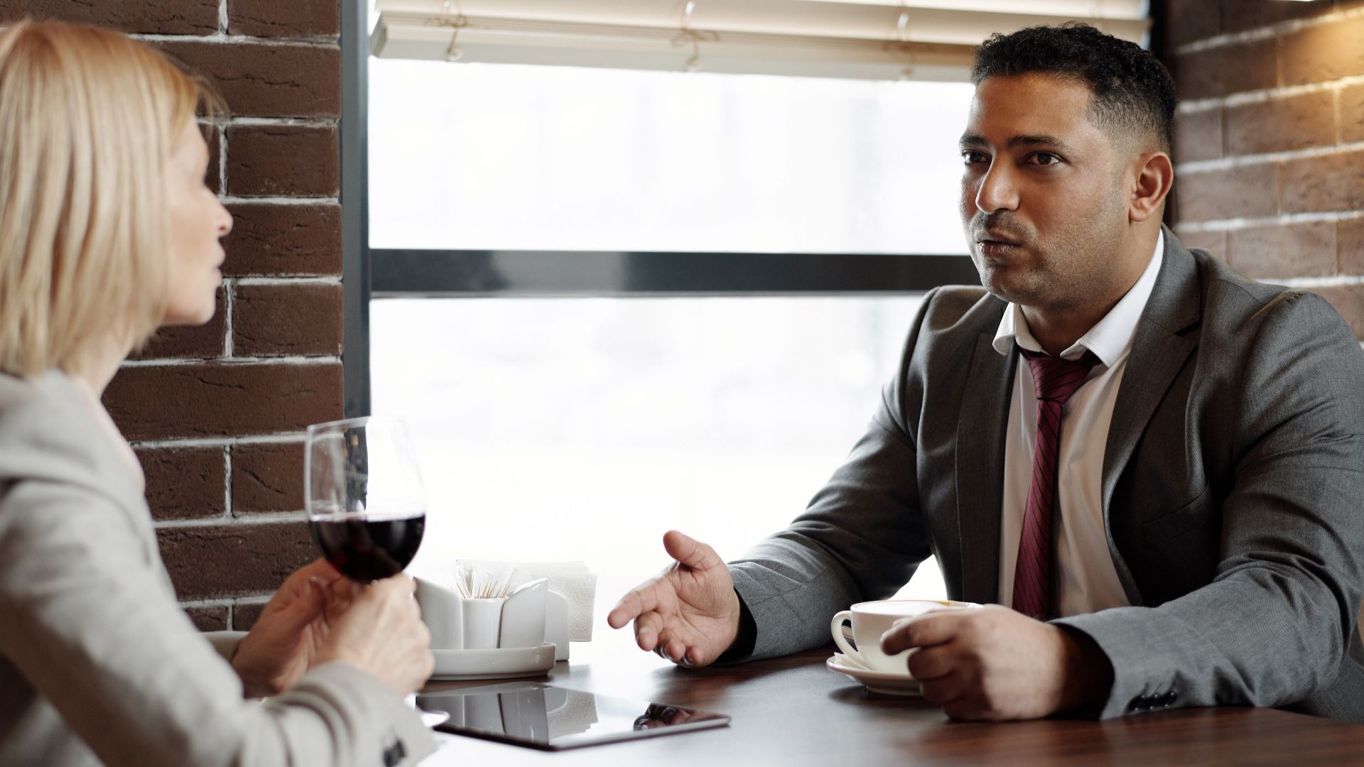 Two business professionals discussing over coffee and wine in a contemporary café.