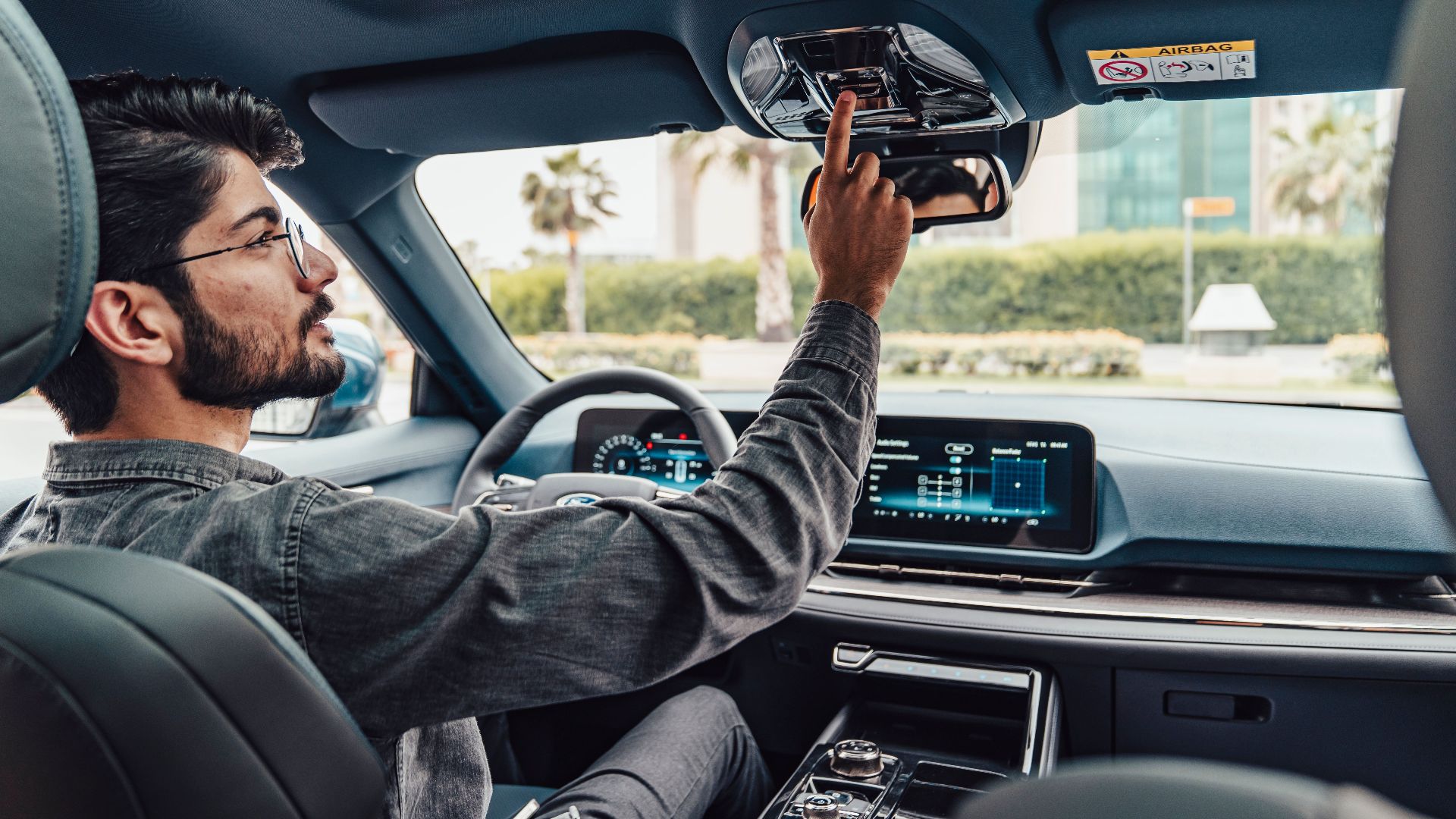 A man adjusts the interior features of a modern car while driving in Erbil, Iraq.