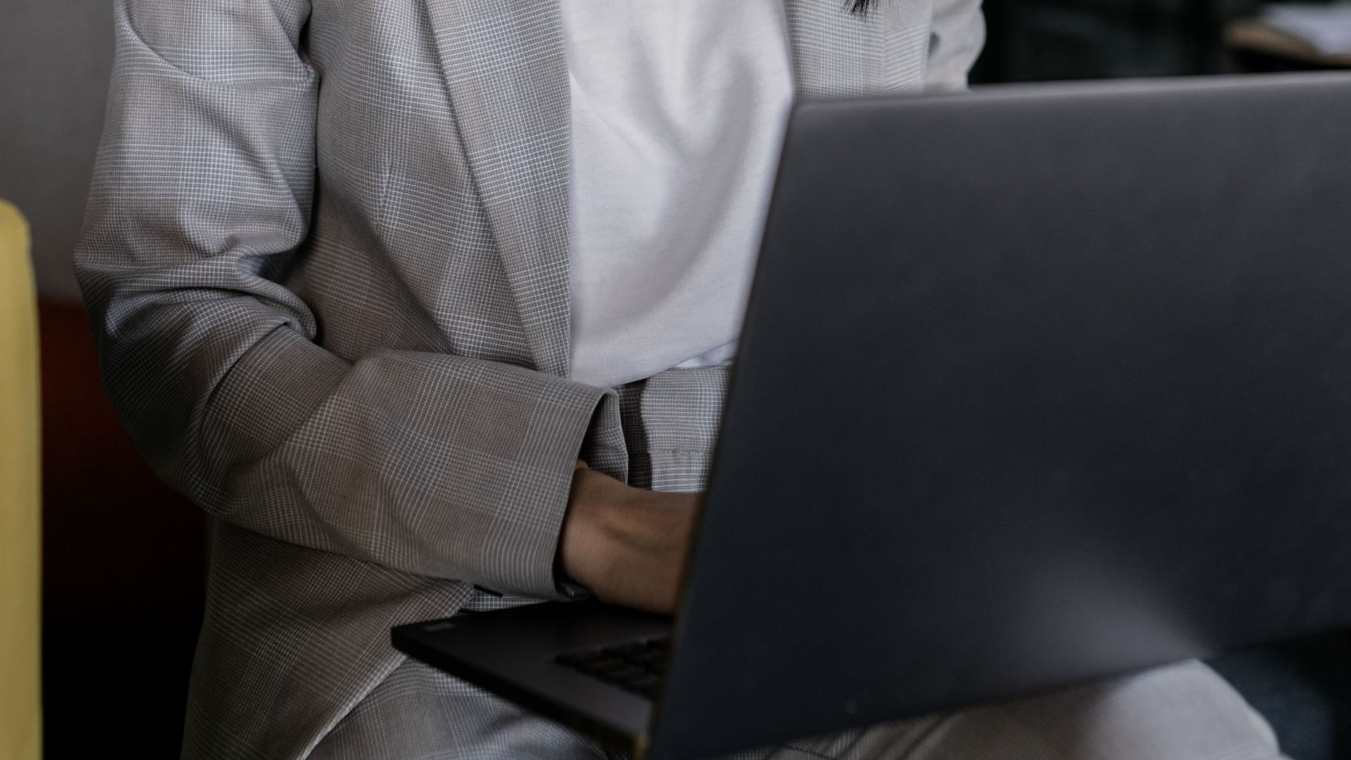 Focused Asian woman in business attire working on laptop in a modern office setting.