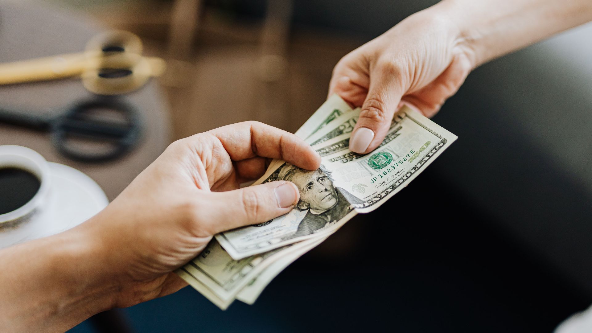 A close-up image of hands exchanging US dollar bills, symbolizing financial transaction or payment.