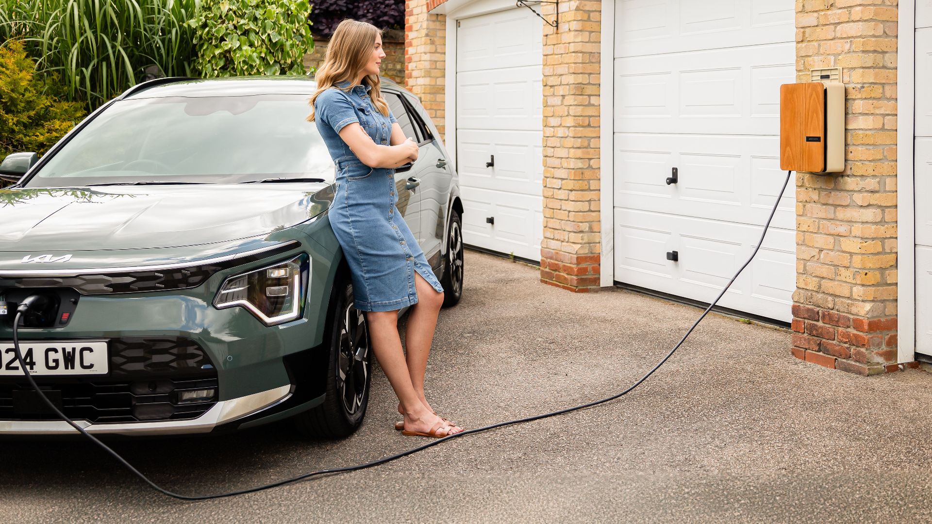 Woman charging electric vehicle at home with a modern wall-mounted charging station.