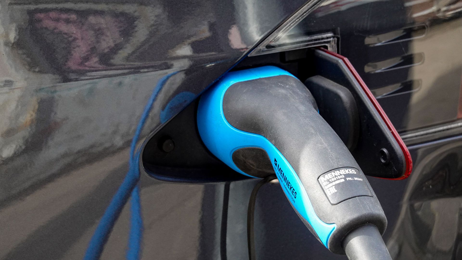 Close-up of an electric vehicle being charged using a Mennekes EV connector.