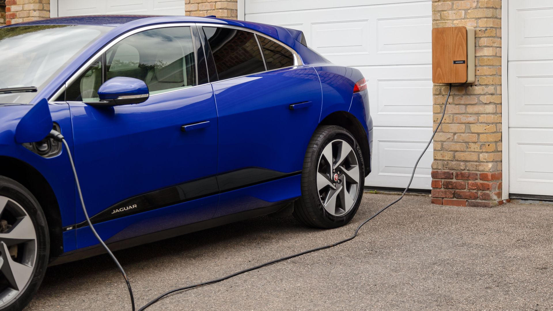 Blue electric vehicle charging at home using wall-mounted unit. Sustainable transportation solution.