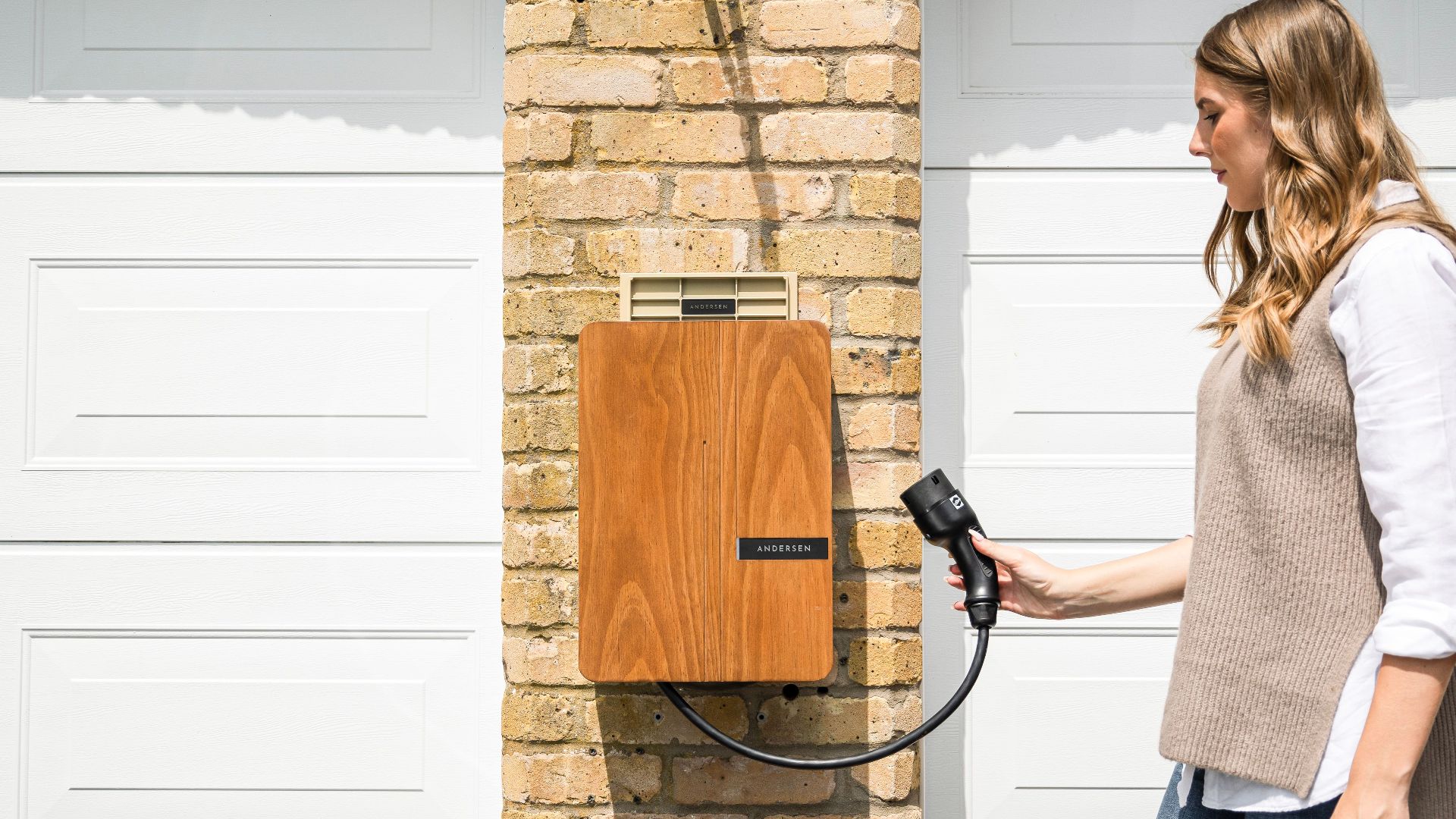 A woman uses a home electric vehicle charger mounted on a brick wall.