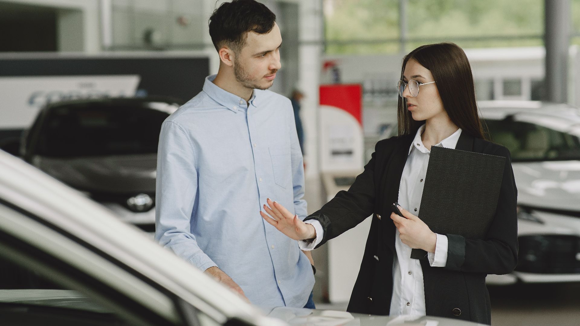 A salesperson and customer discussing car features in a dealership setting.