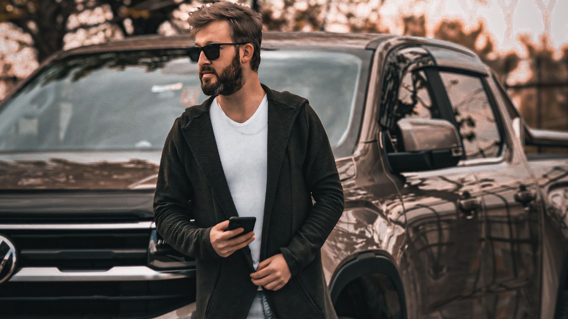 Stylish man with sunglasses and smartphone leaning against a Volkswagen pickup truck outdoors.