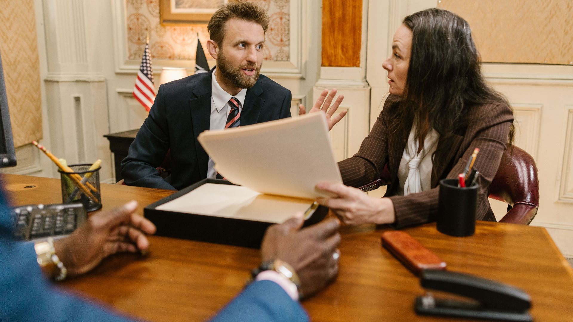Diverse group in a corporate office engaged in a formal meeting. Professional attire and documents suggest a business discussion.
