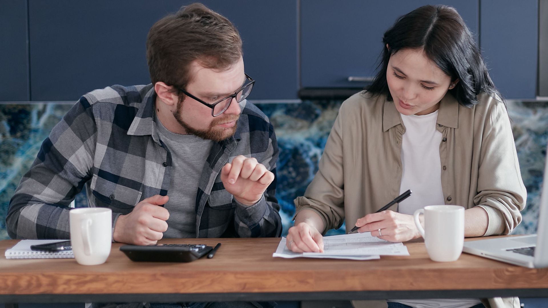 A couple sitting at a wooden table reviewing documents and discussing finances.