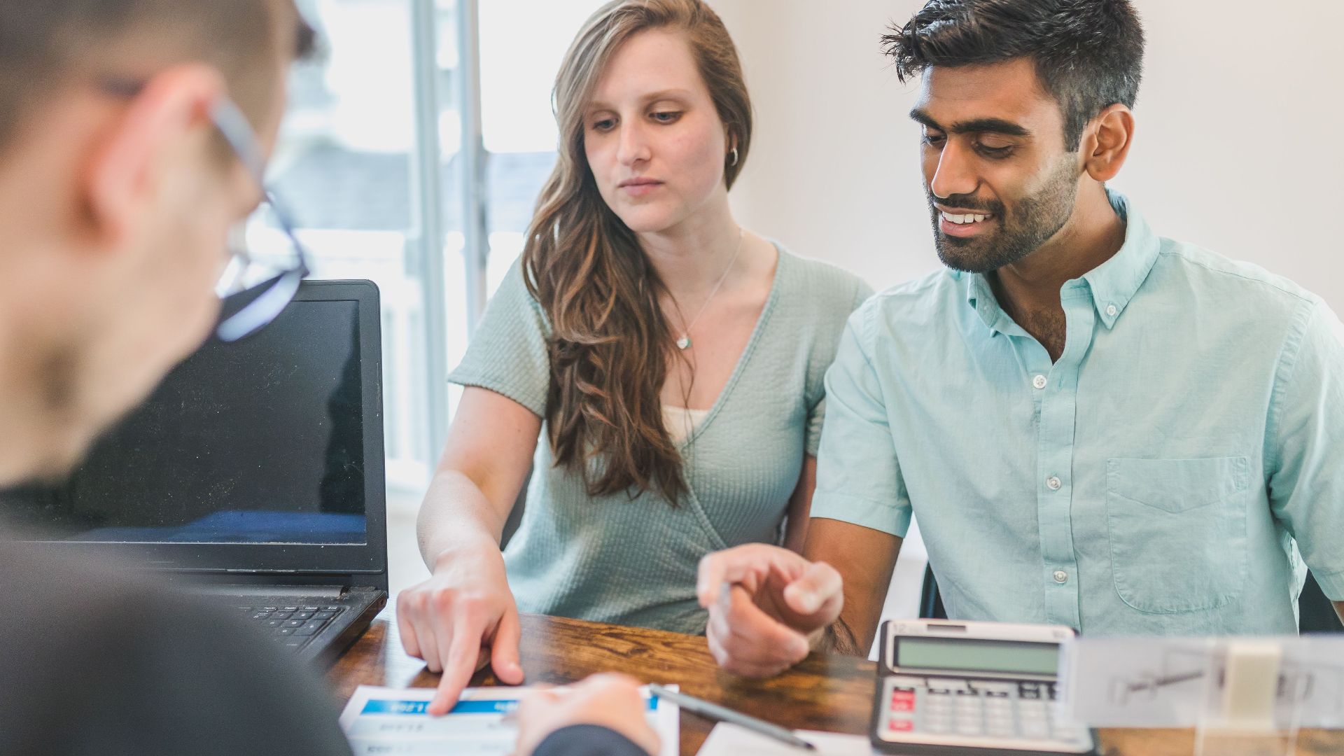 Young couple consulting with a financial advisor using a calculator and documents in a bright office setting.