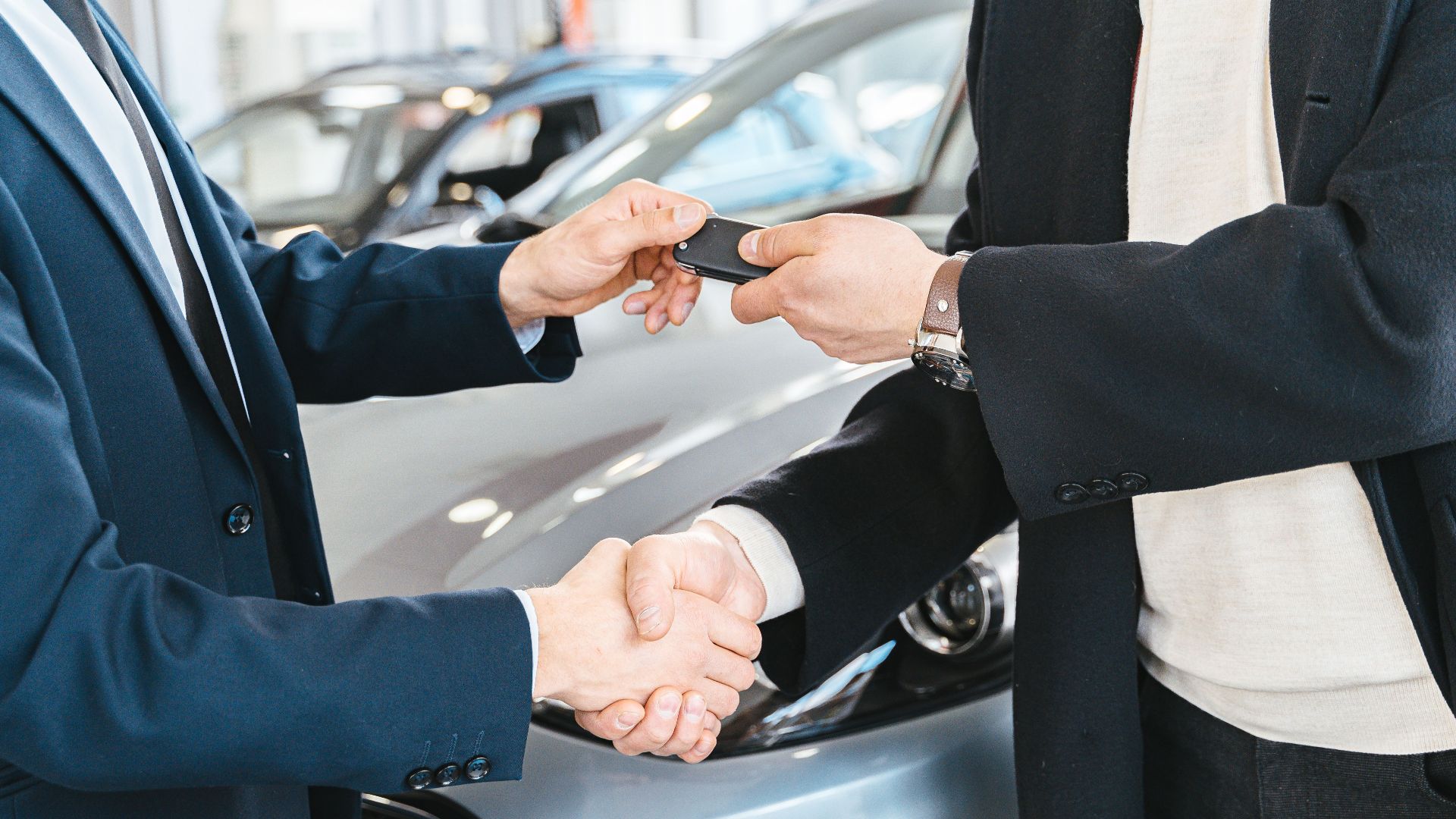 Two businessmen shaking hands and exchanging car keys in a dealership. Symbolizes a successful deal.