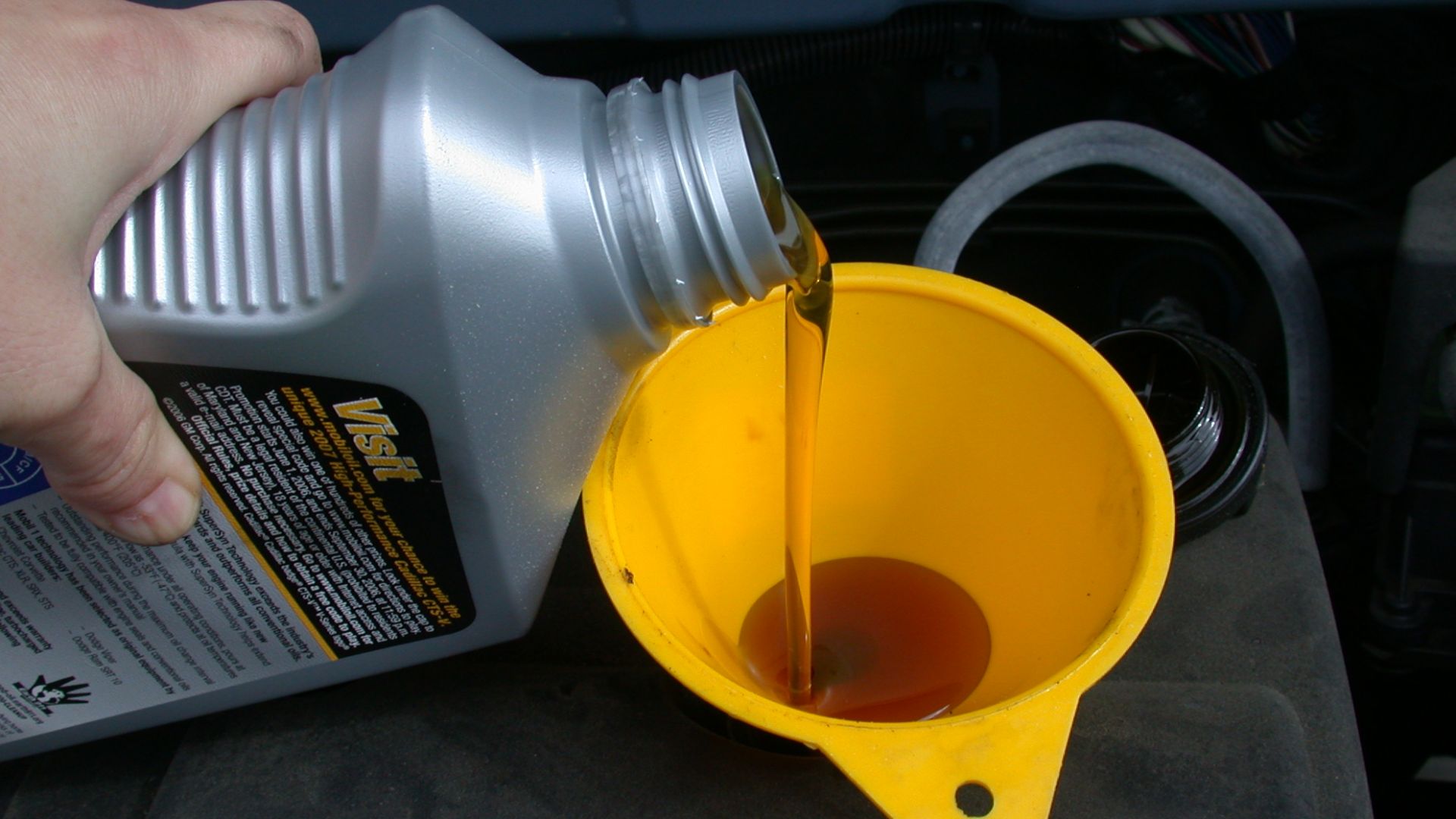 Using a funnel to refill the motor oil in an automobile as part of an oil change.