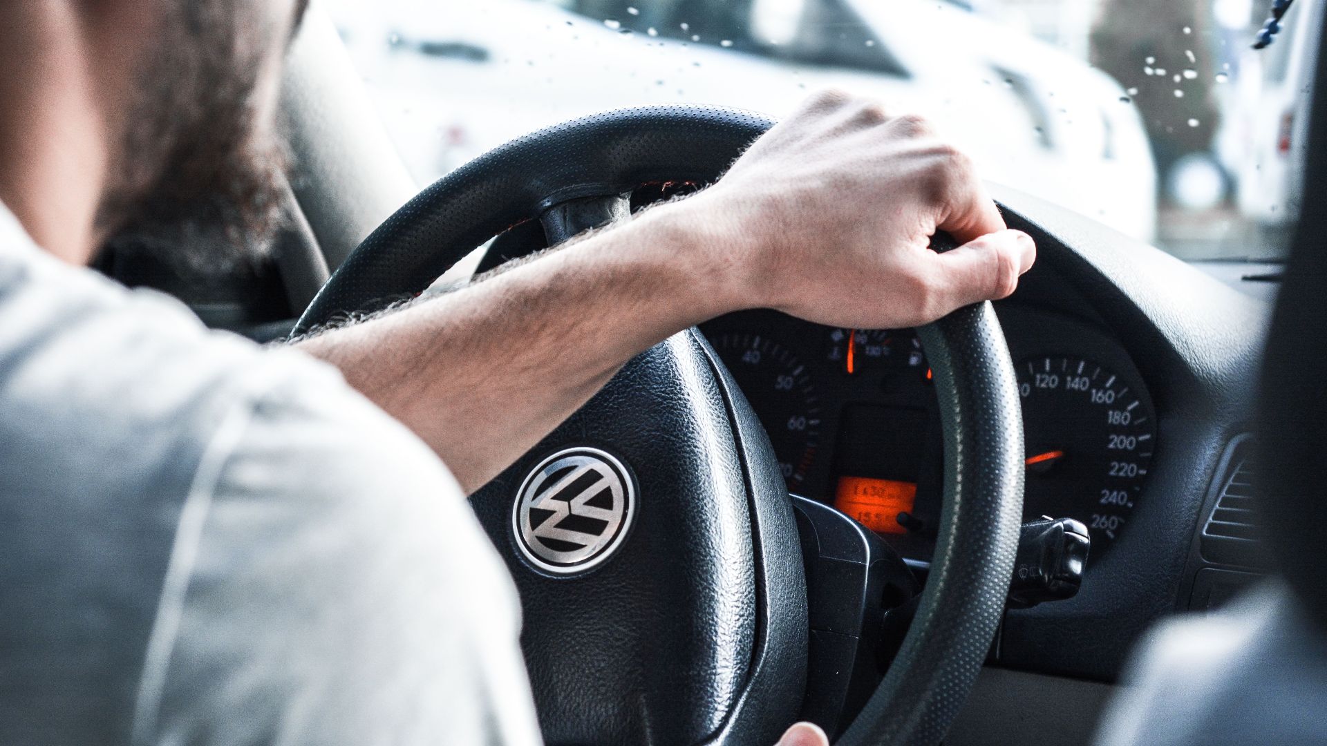 Man gripping Volkswagen steering wheel, focused on driving and vehicle interior details.