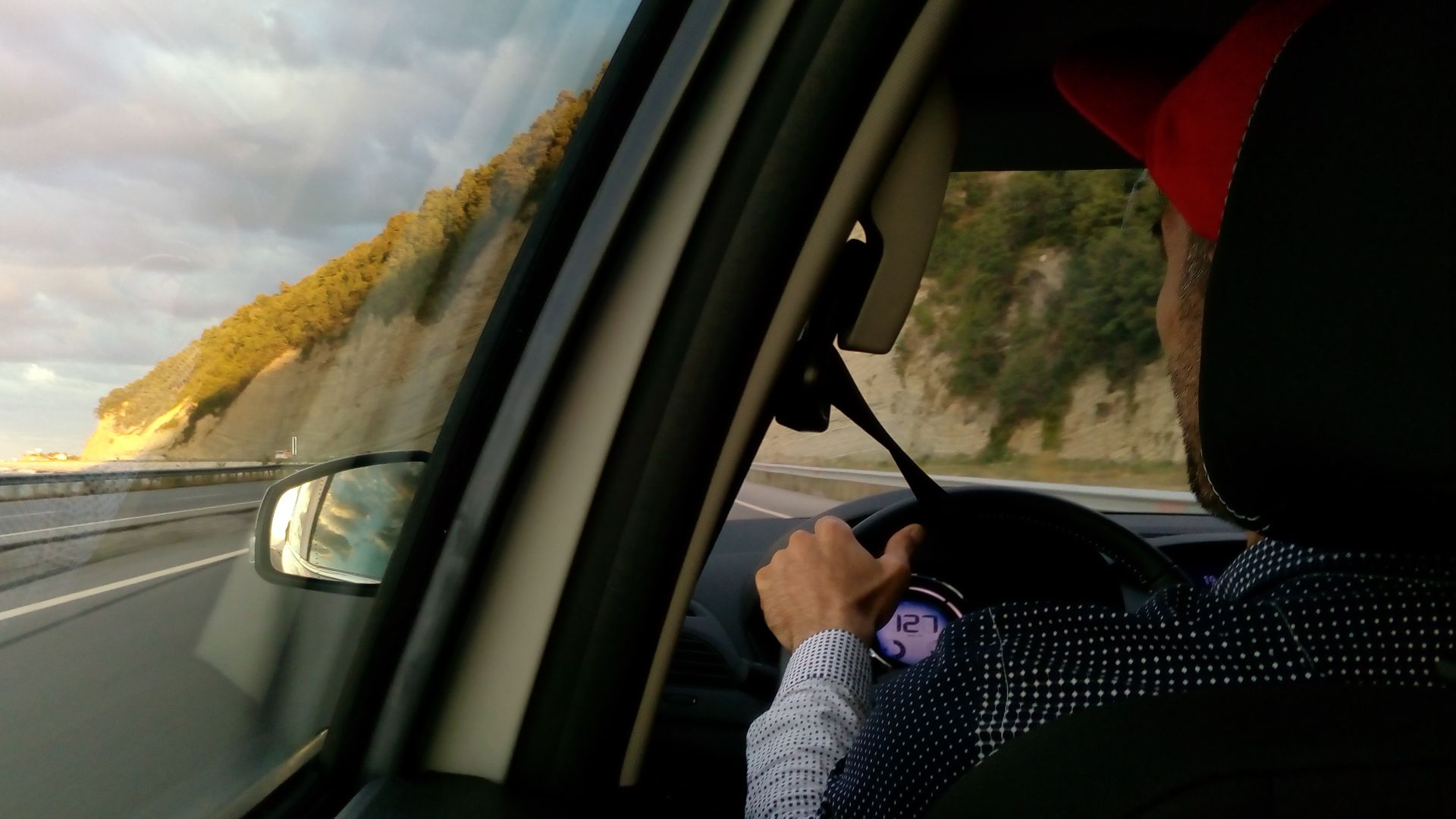 a shot from the backseat of a man in a red hat driving a car on the road
