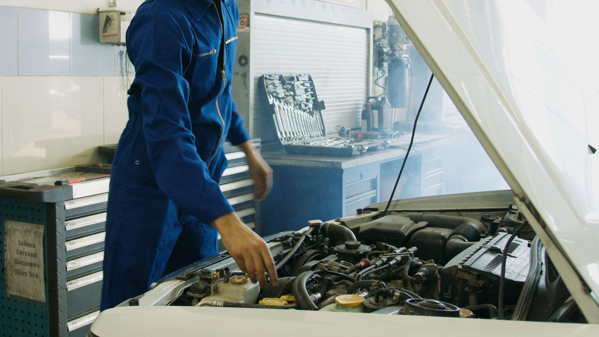 Mechanic in blue uniform inspecting a car engine in a workshop.