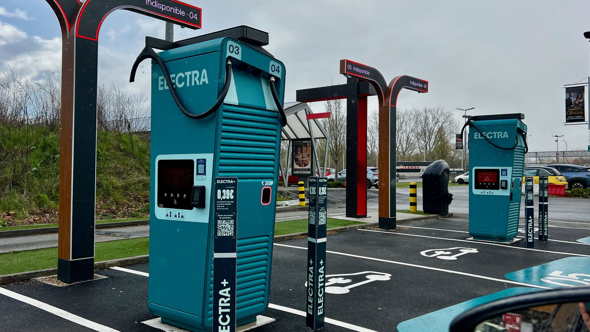 A modern electric vehicle charging station in a parking lot on a cloudy day.