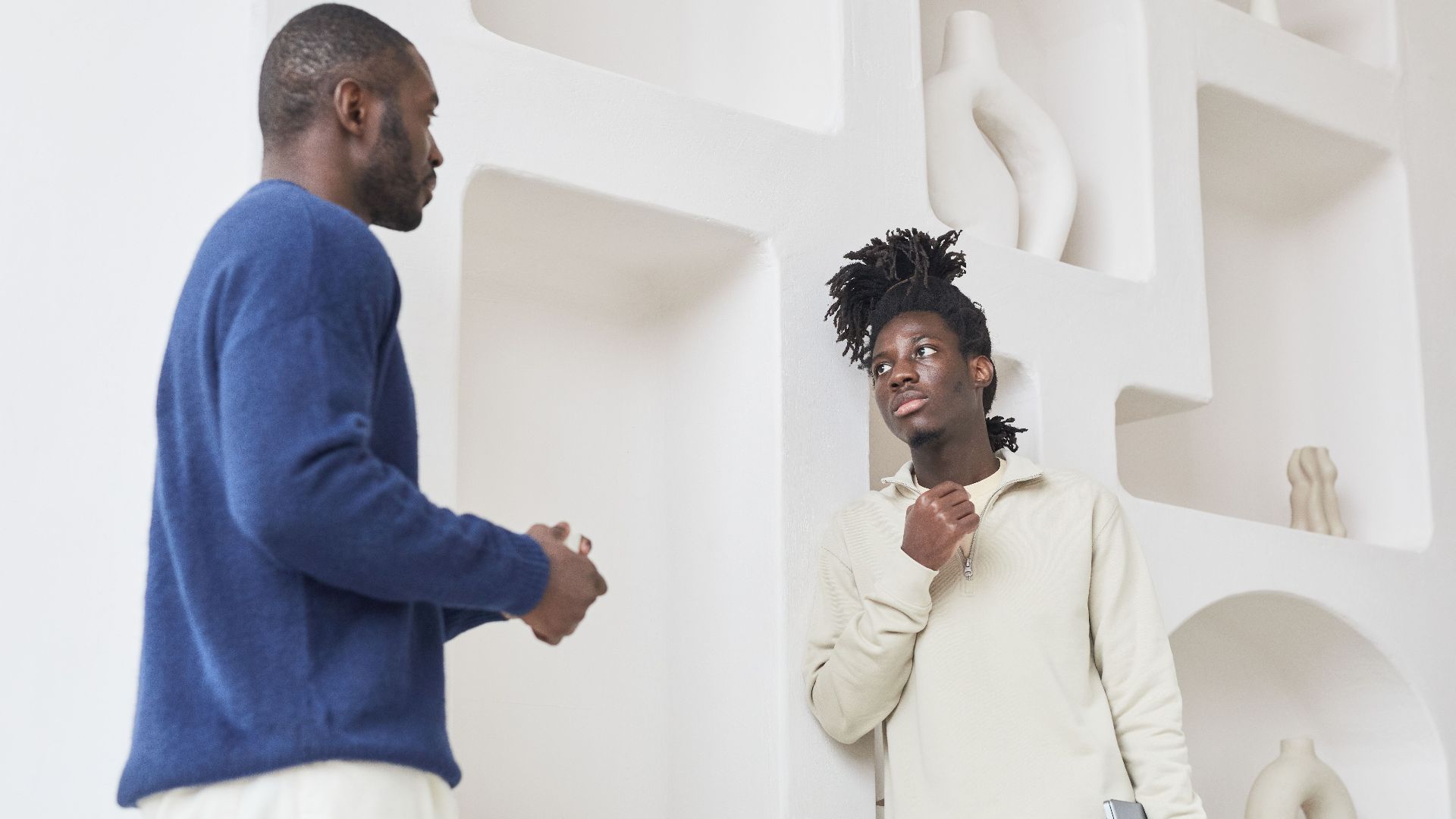 Two men in conversation against a modern interior backdrop, discussing ideas creatively.