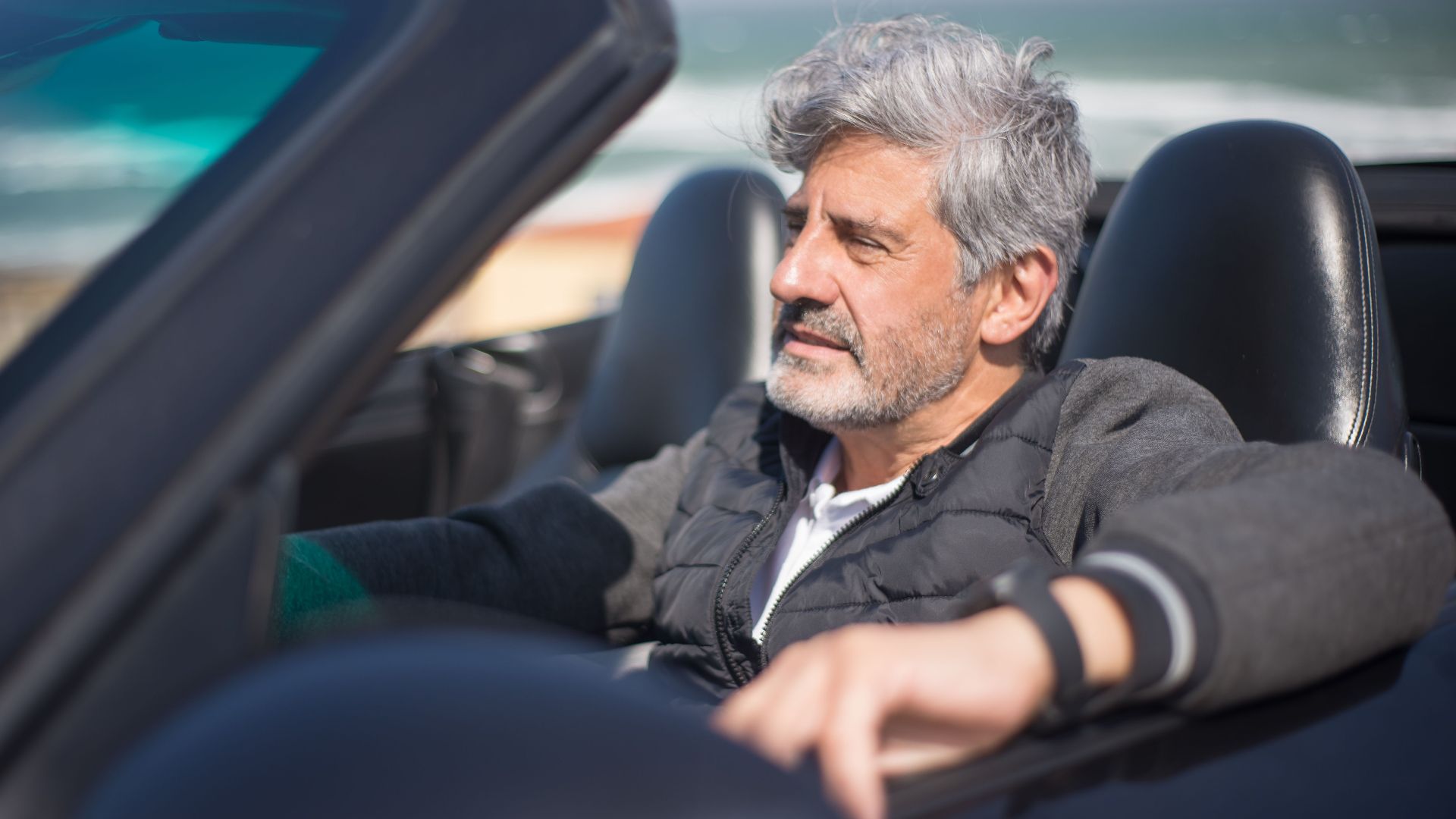 Senior man enjoying a road trip along a scenic coastal drive in a convertible car.