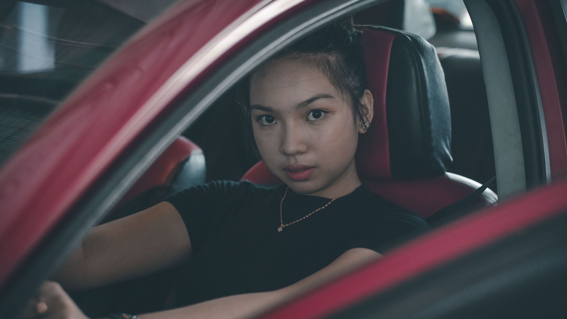 A determined young woman sitting in the driver's seat of a car, ready to drive.