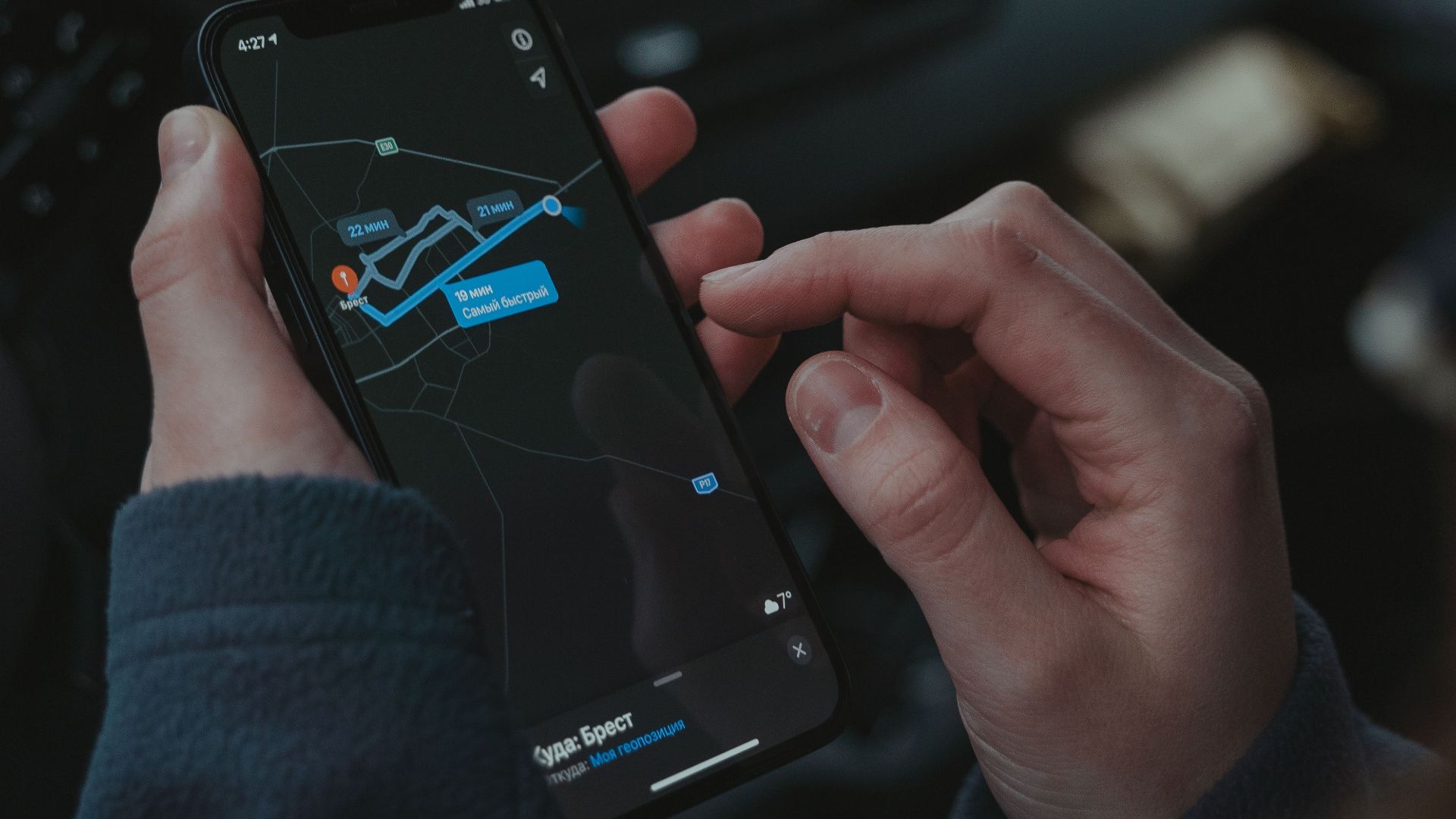 Close-up of a person using a smartphone for GPS navigation inside a car, showing the screen with a route.