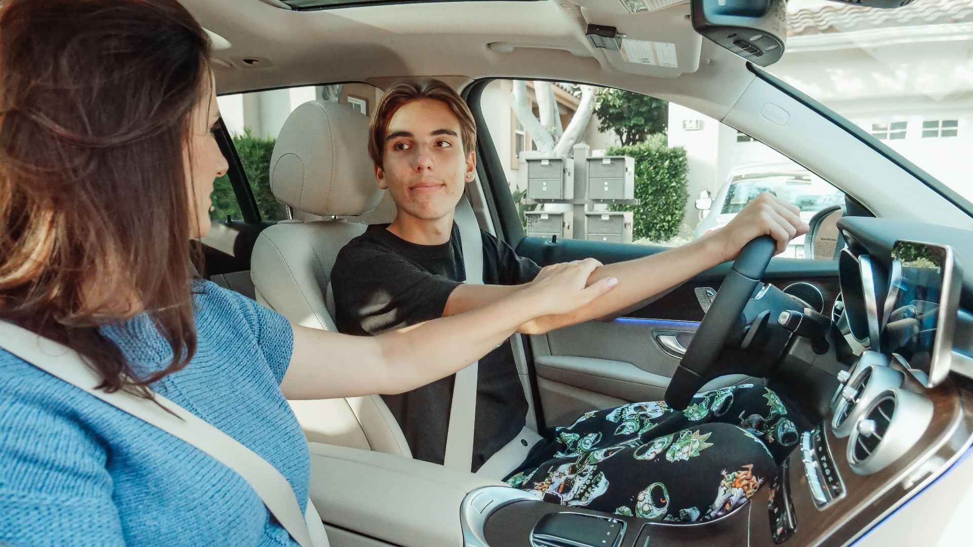 A mother supports her teenage son as he learns to drive in a car