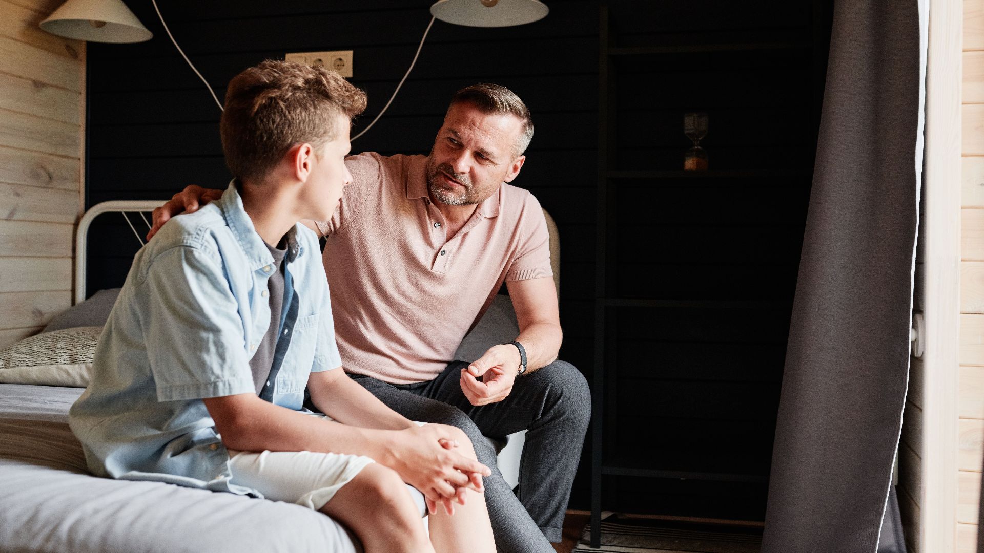 A father bonding with his teenage son in a cozy bedroom, sharing advice and conversation.