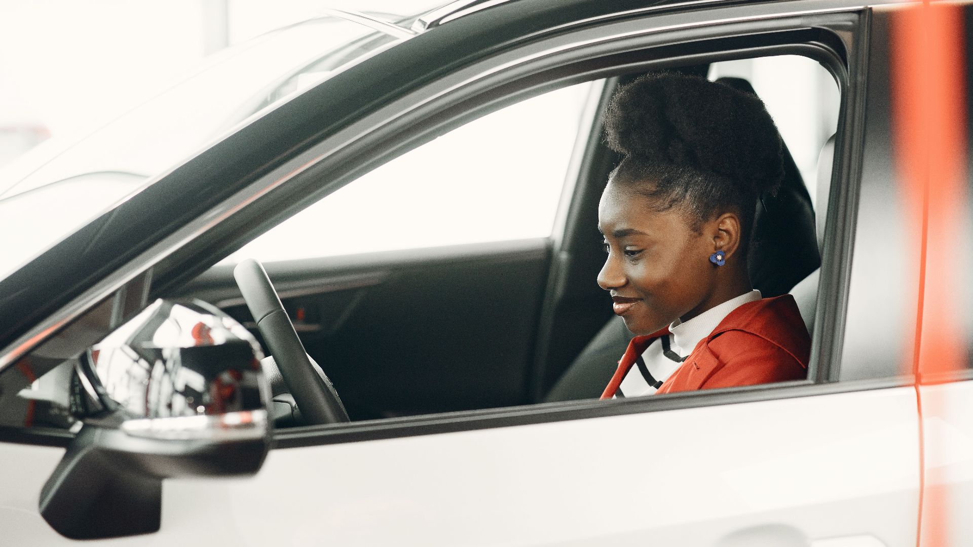 A young African American woman smiling while sitting inside a parked car.