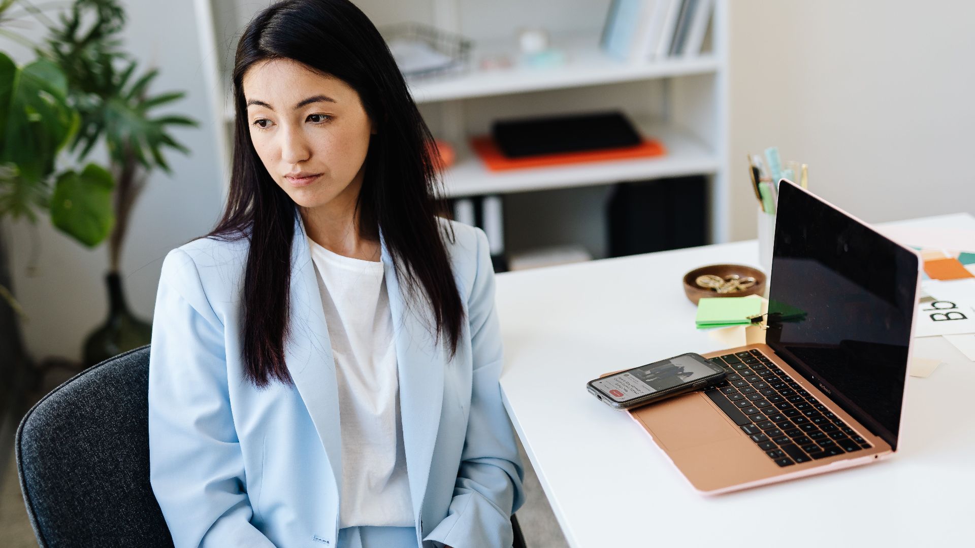 Professional woman in blue blazer sitting at a desk with laptop and smartphone.