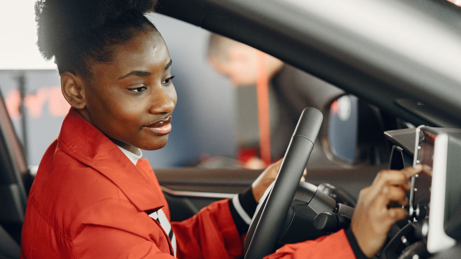Young woman in red coat using touch screen in car interior.