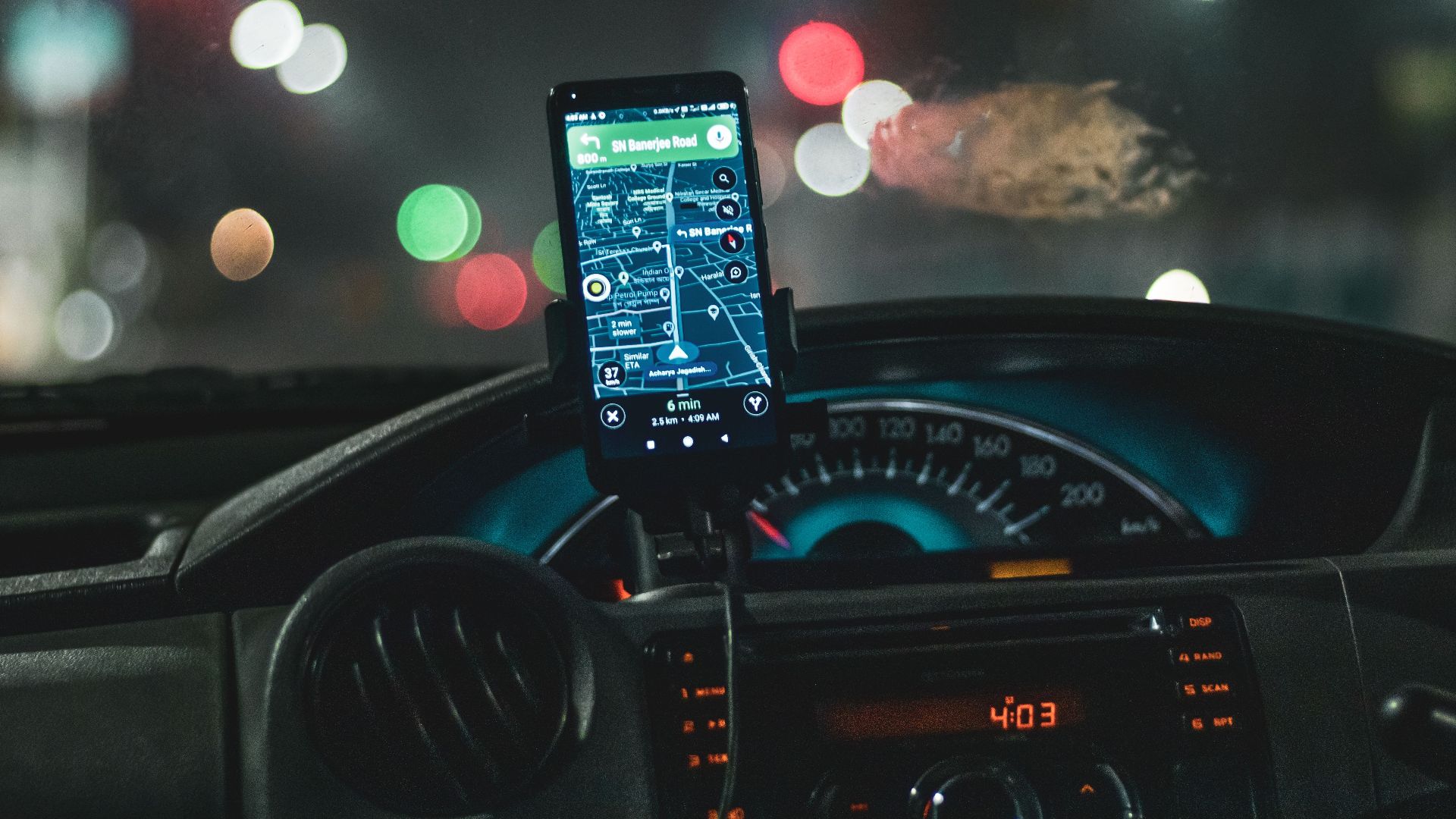 Close-up of a smartphone with map navigation in a car at night with bokeh effect.