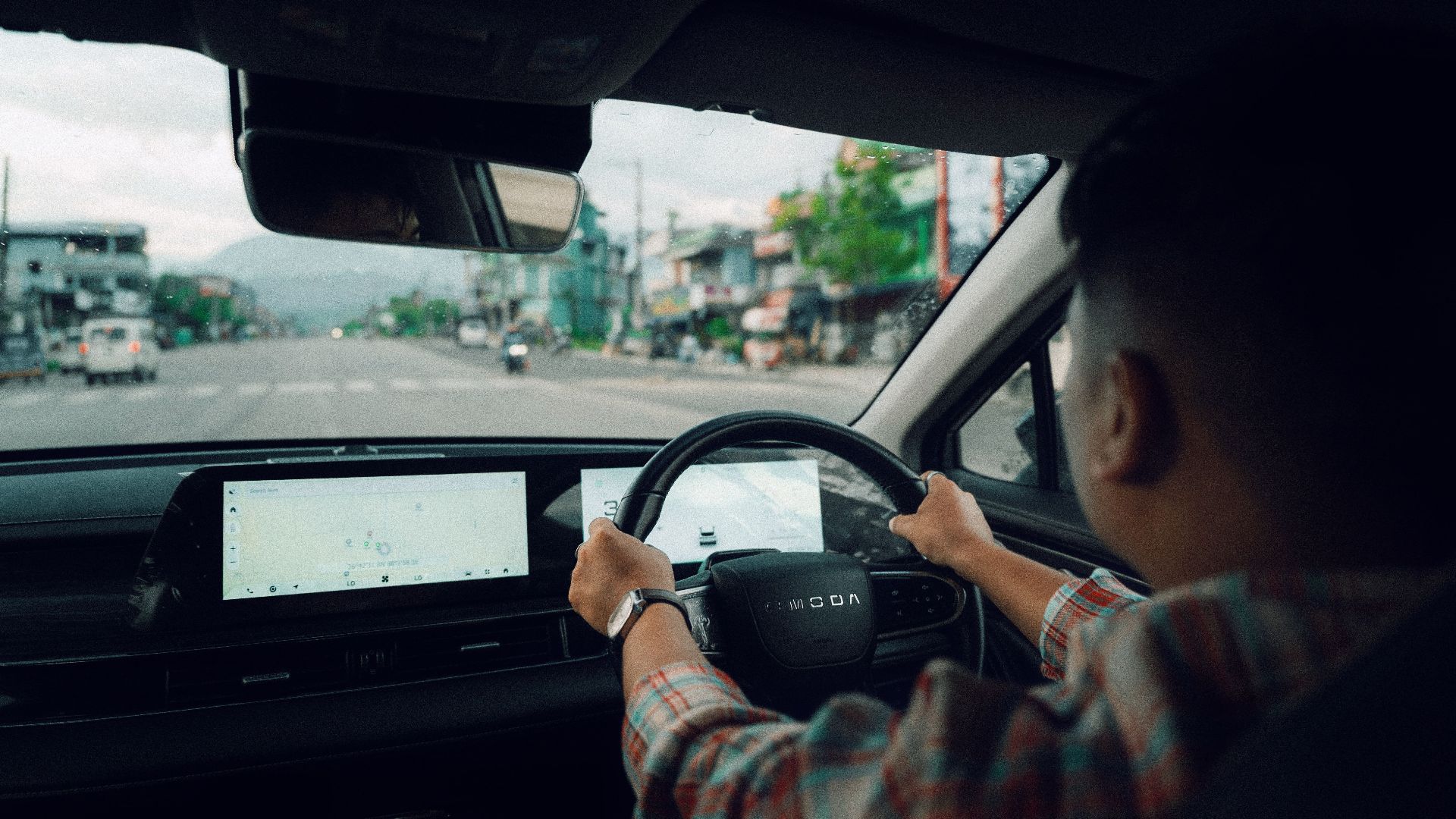 Person driving a modern car through town, showing dashboard and road view.