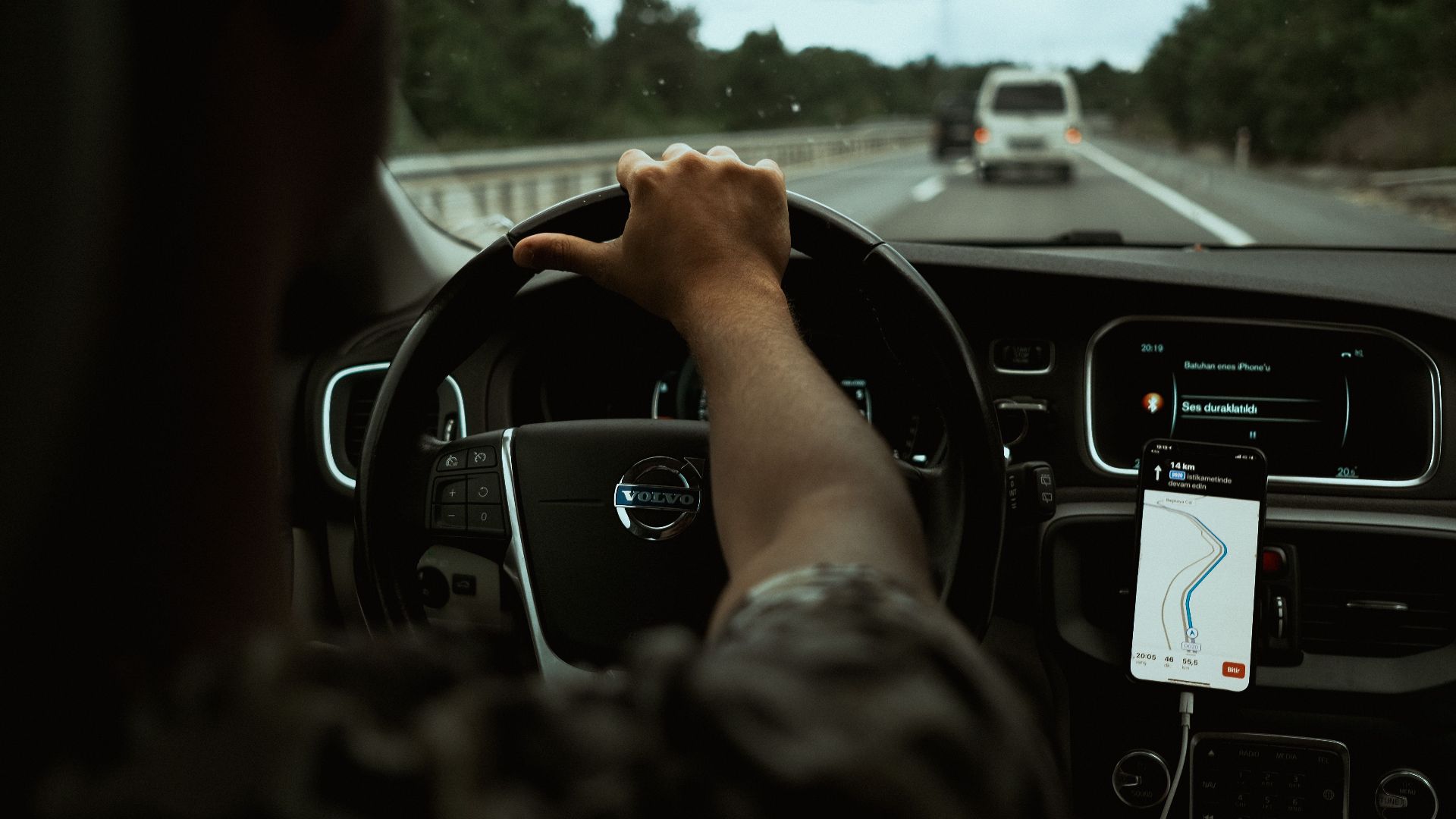 A driver navigates the highway with a smartphone GPS, showcasing modern car interior design.
