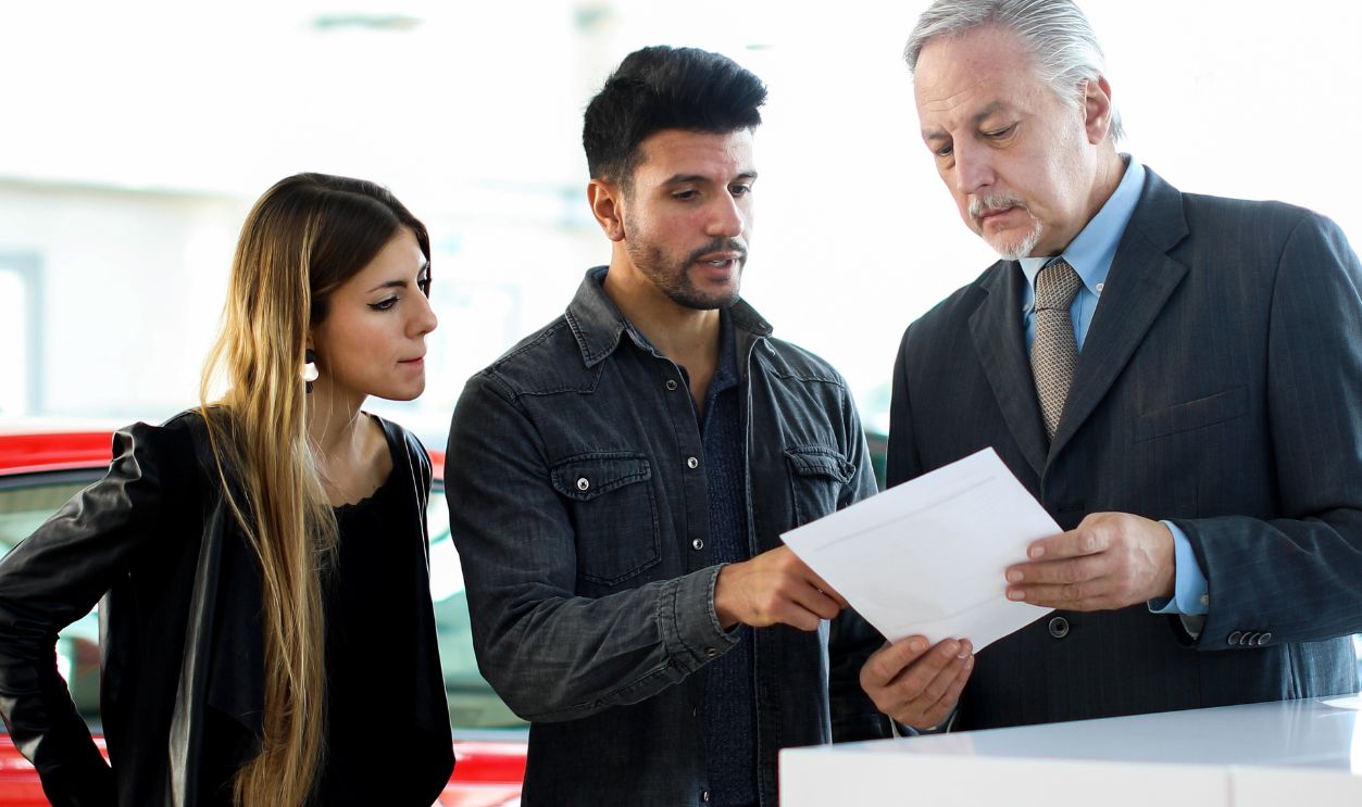 Car dealer reading a contract to a couple in an auto showroom