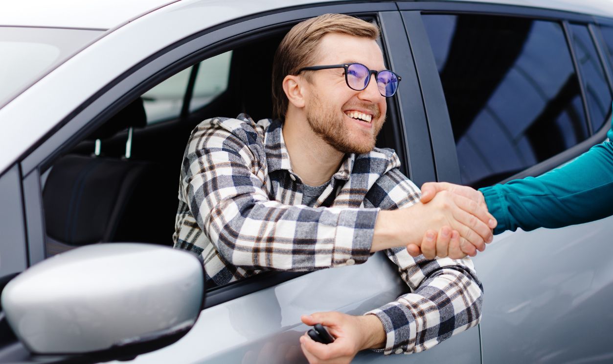 Man buying car and shaking hands with salesman against blurred auto, closeup. Concept of choosing and buying new car at showroom.