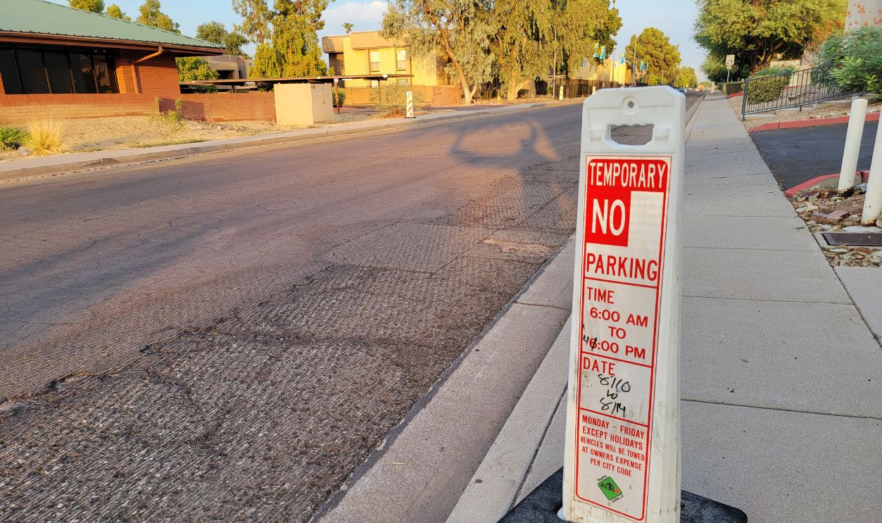Phoenix, AZ - August 10, 2026: A vertical white plastic temporary no parking sign sits on a concrete sidewalk curb next to a milled asphalt road in a quiet residential neighborhood