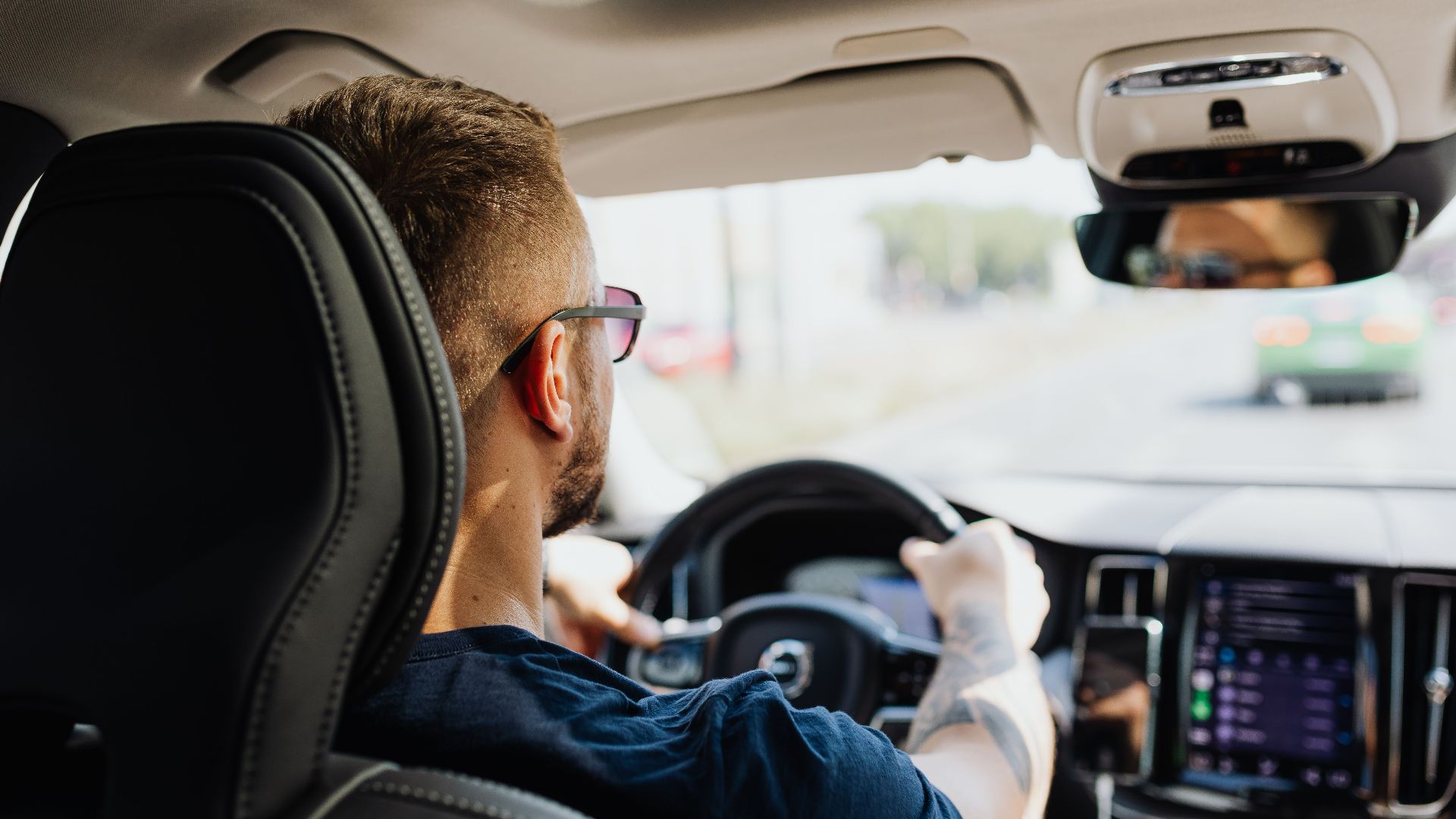 Rear view of a man driving a car with focus on interior details and steering.
