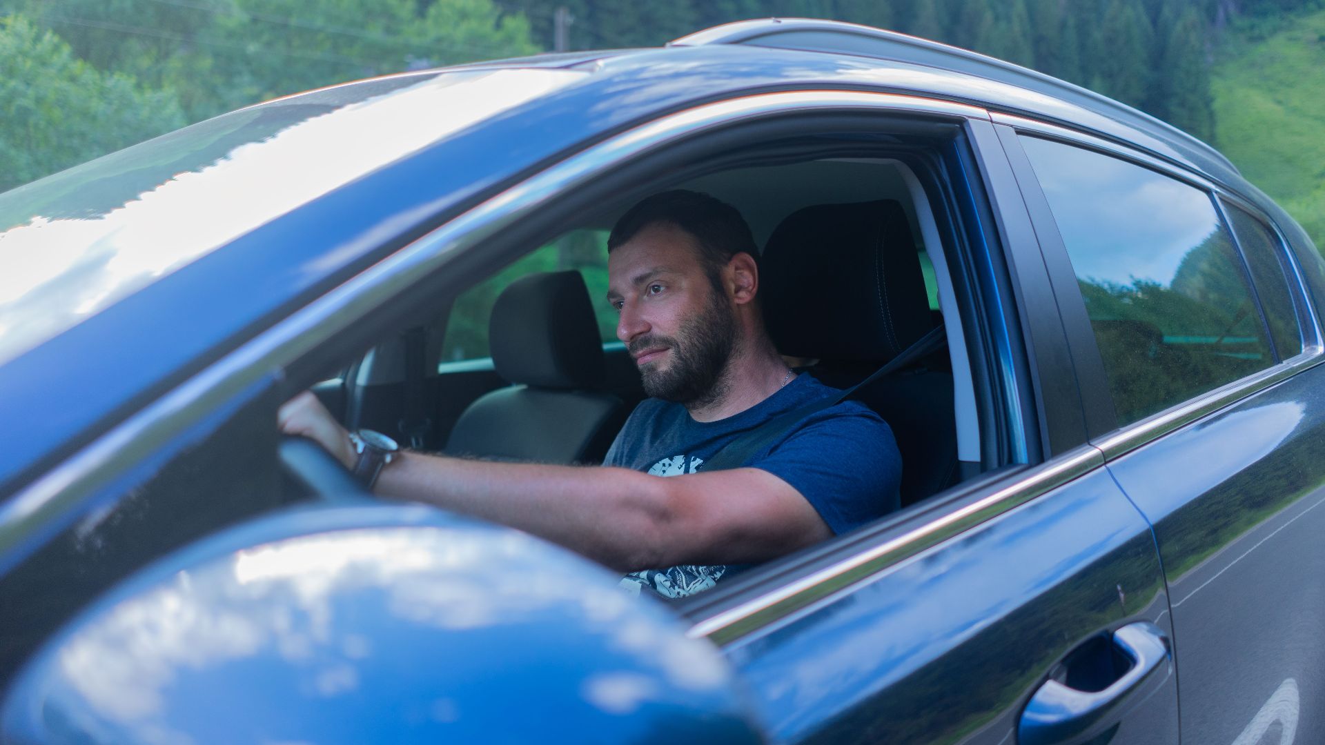 Bearded man enjoying a drive through lush green countryside on a sunny day.
