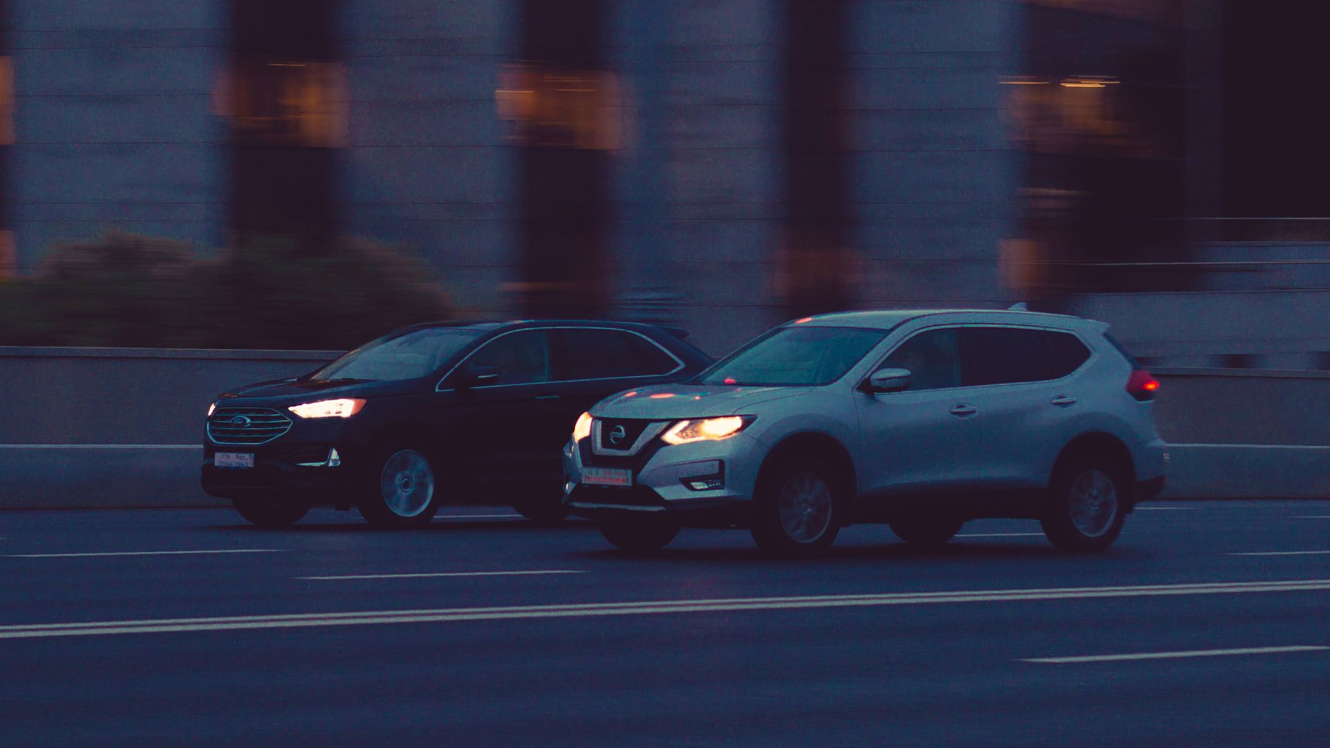 Two suvs drive on a road at dusk