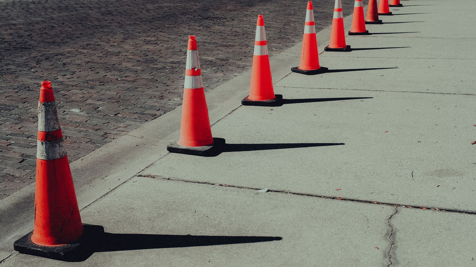 A row of bright orange traffic cones on sunlit pavement casting long shadows.
