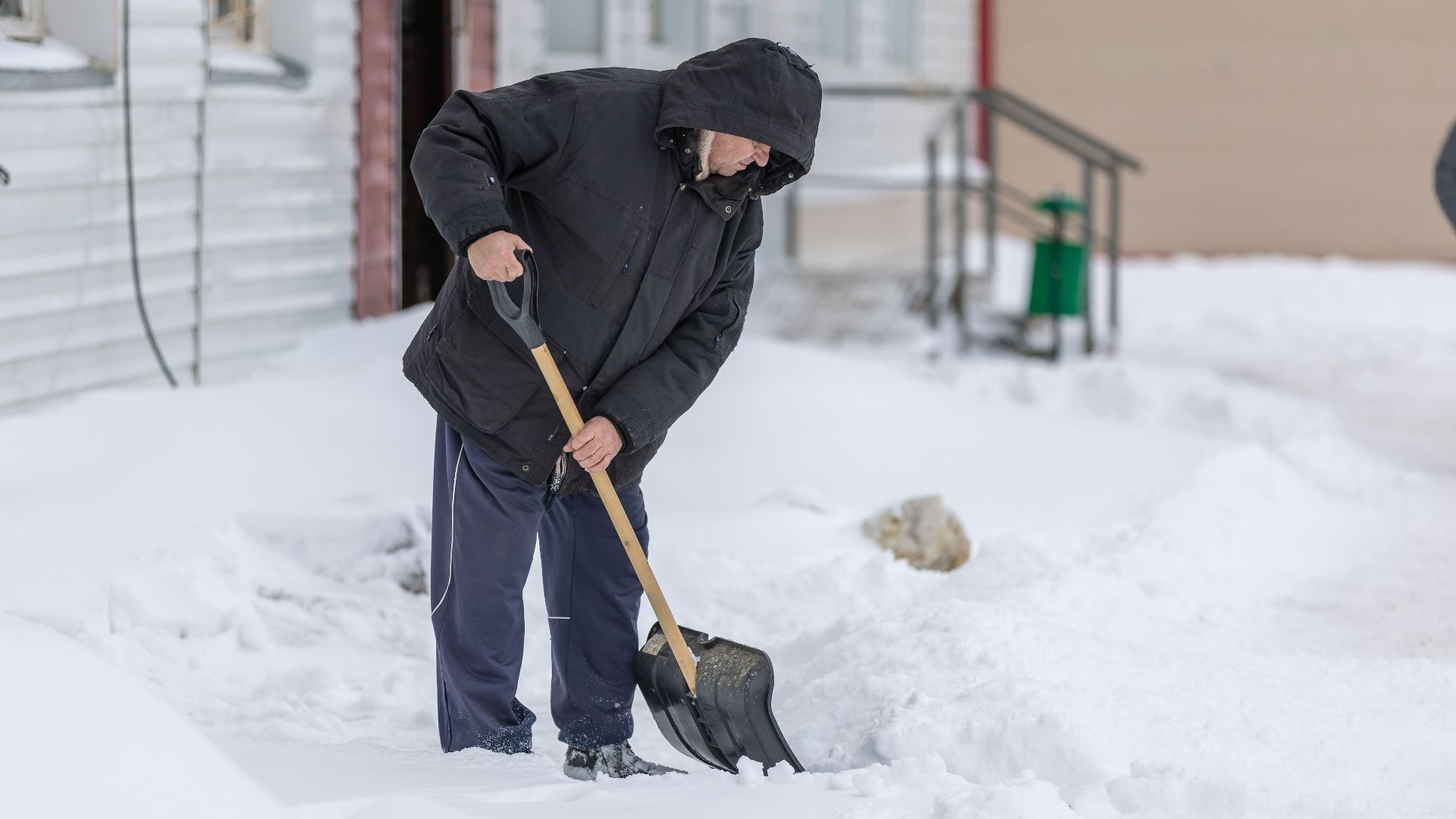 Adult man clearing snow with a shovel during a cold winter day, showcasing winter weather activities.