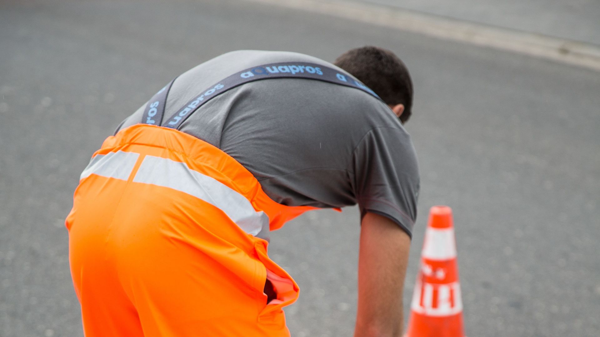 A worker in a fluorescent suit performing road maintenance at a crosswalk with cones.