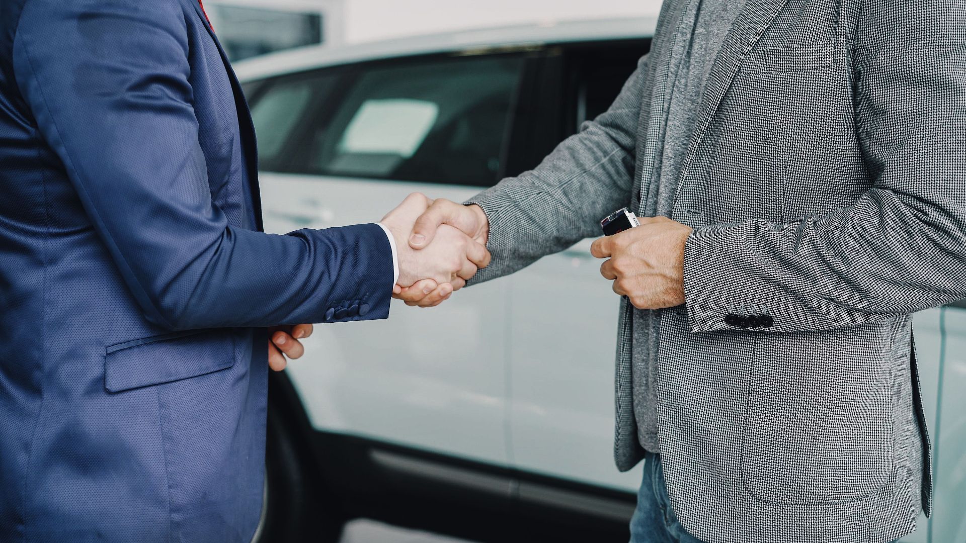 Two businessmen shaking hands in a car dealership, sealing a deal.